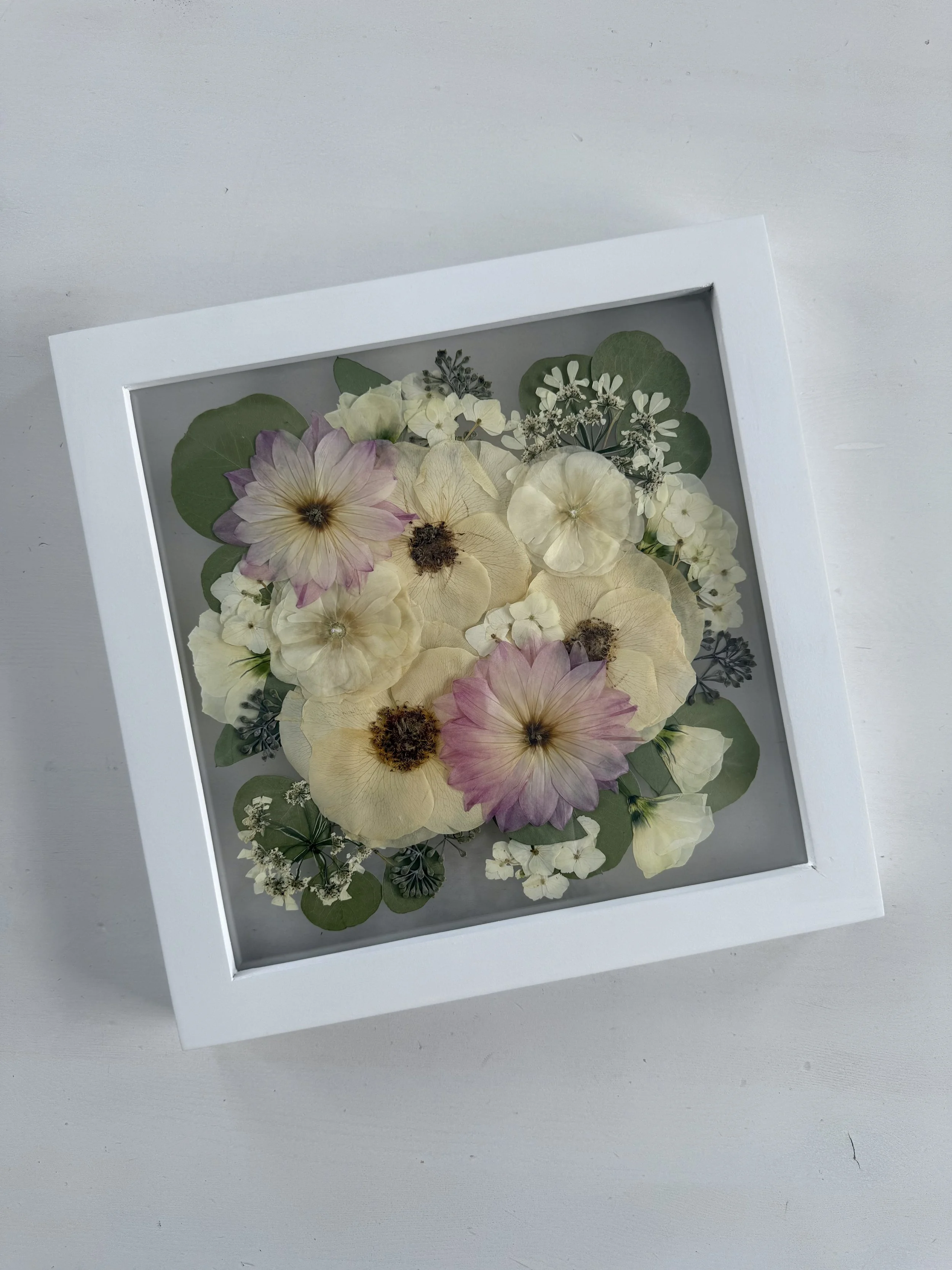 Framed pressed wedding bouquet flowers preserved in a floating glass frame.