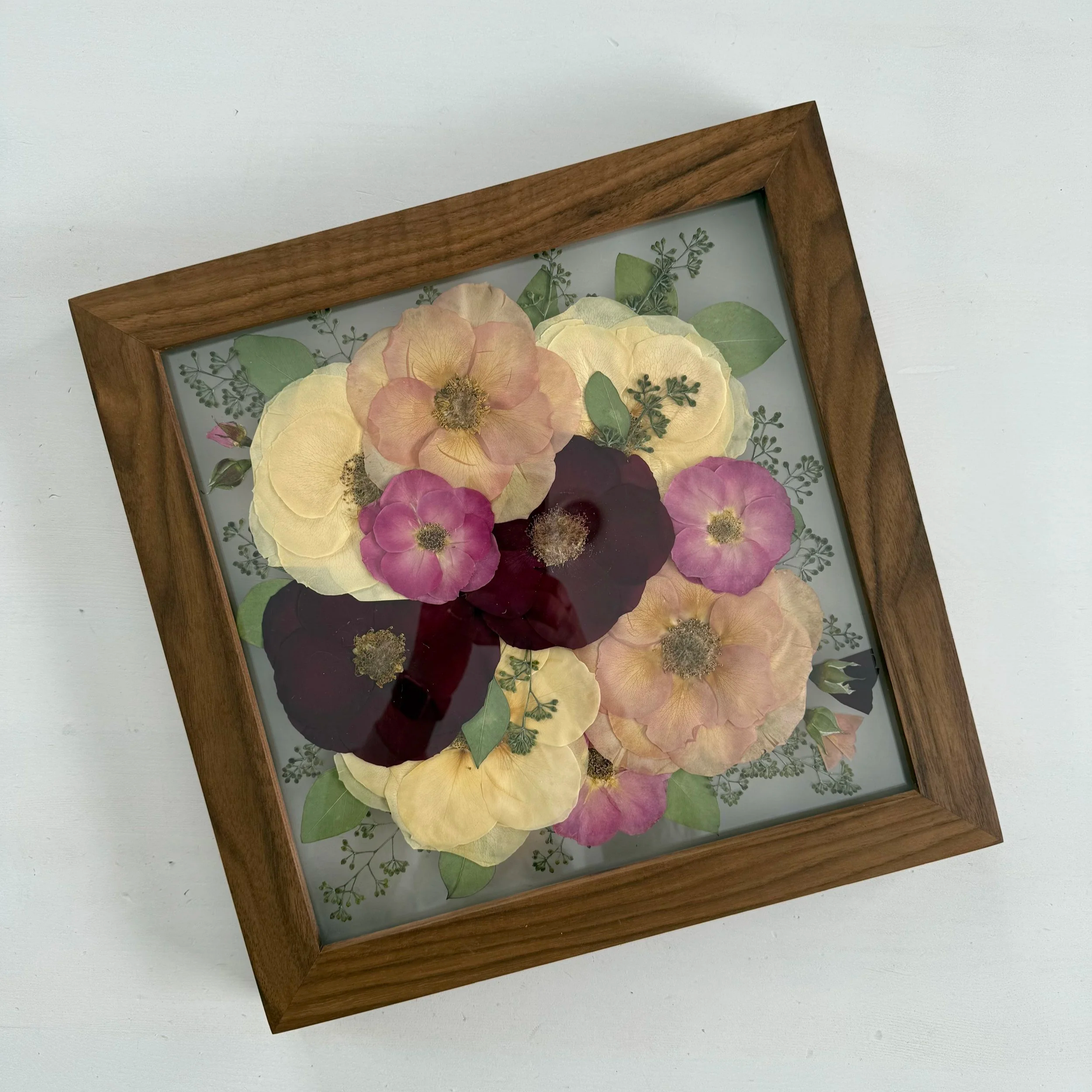 Framed pressed wedding bouquet flowers preserved in a floating glass frame.