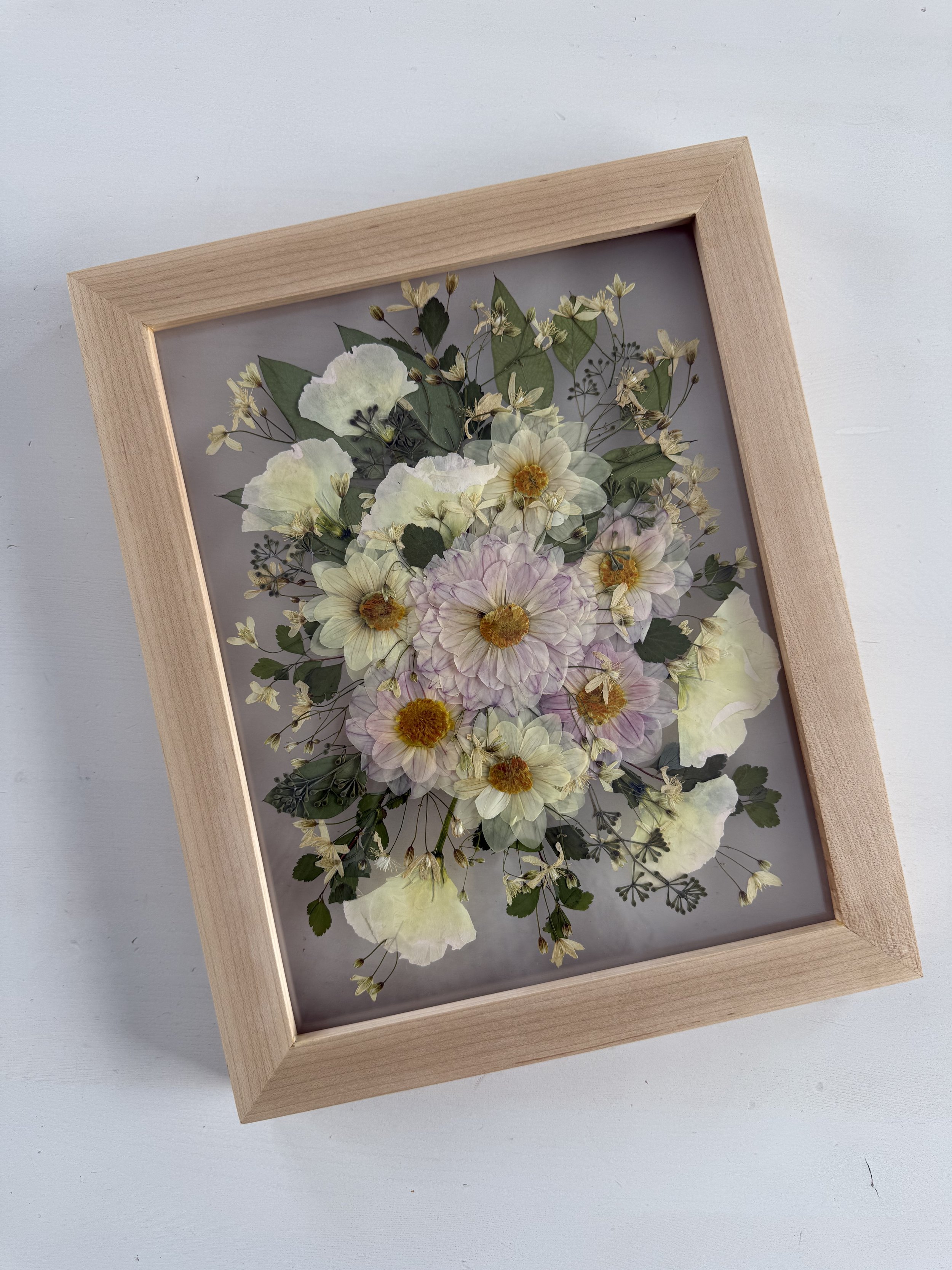 Framed pressed wedding bouquet flowers preserved in a floating glass frame.