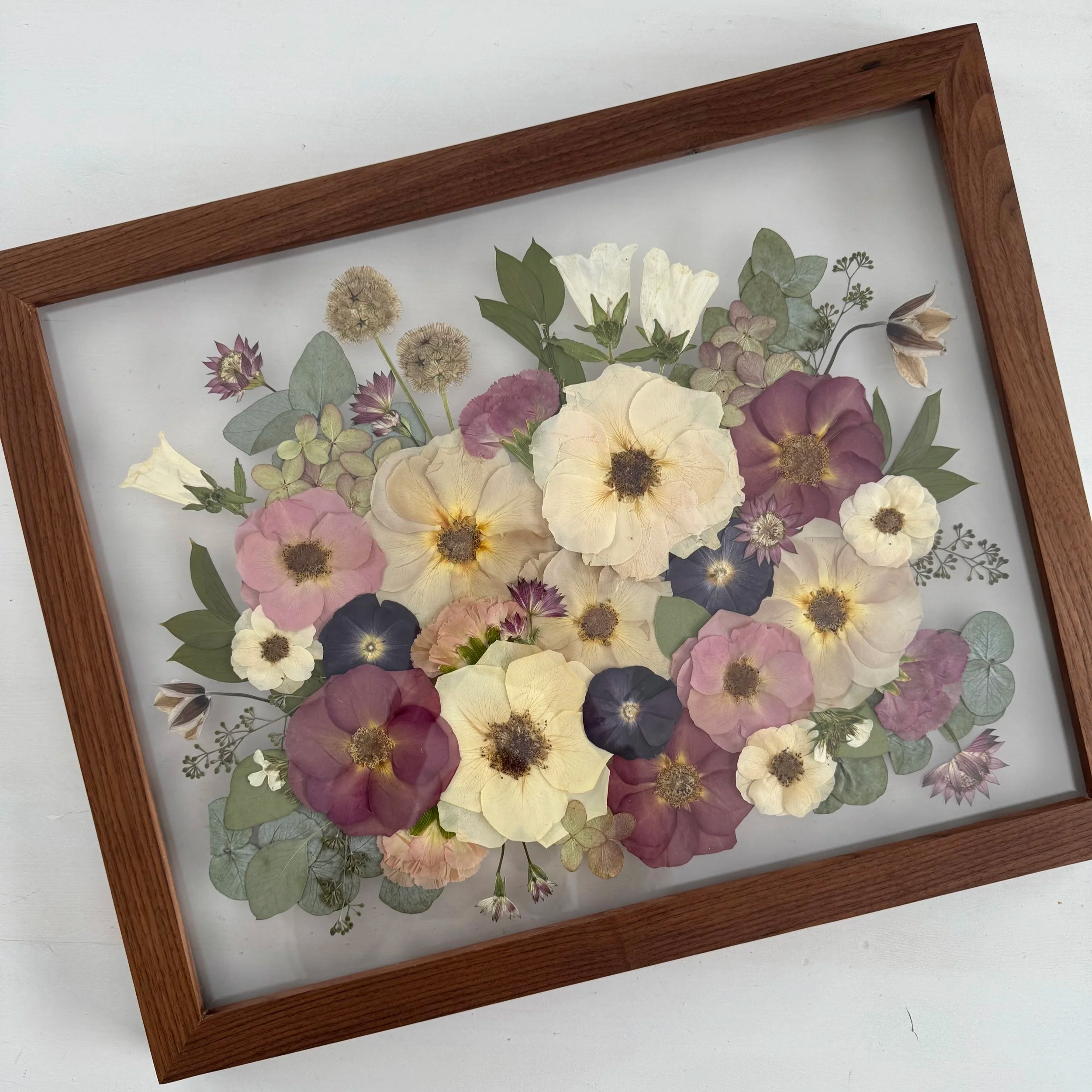 Framed pressed wedding bouquet flowers preserved in a floating glass frame.