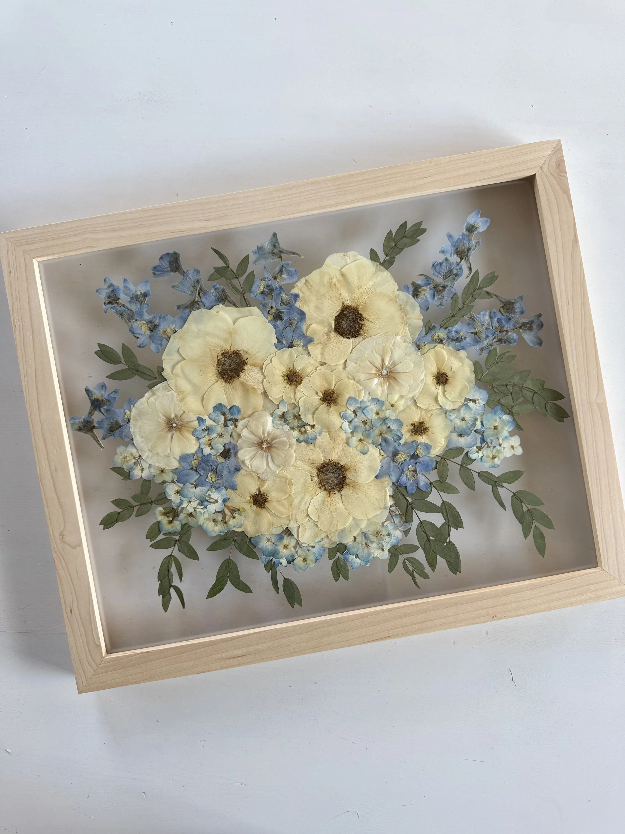 White rose and blue delphinium bridal bouquet flowers, pressed and framed in a bouquet design.