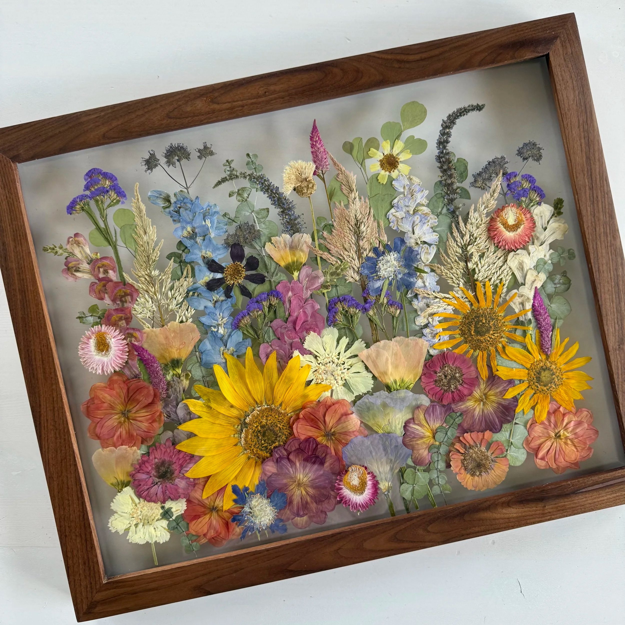 Framed pressed wedding bouquet flowers preserved in a floating glass frame.