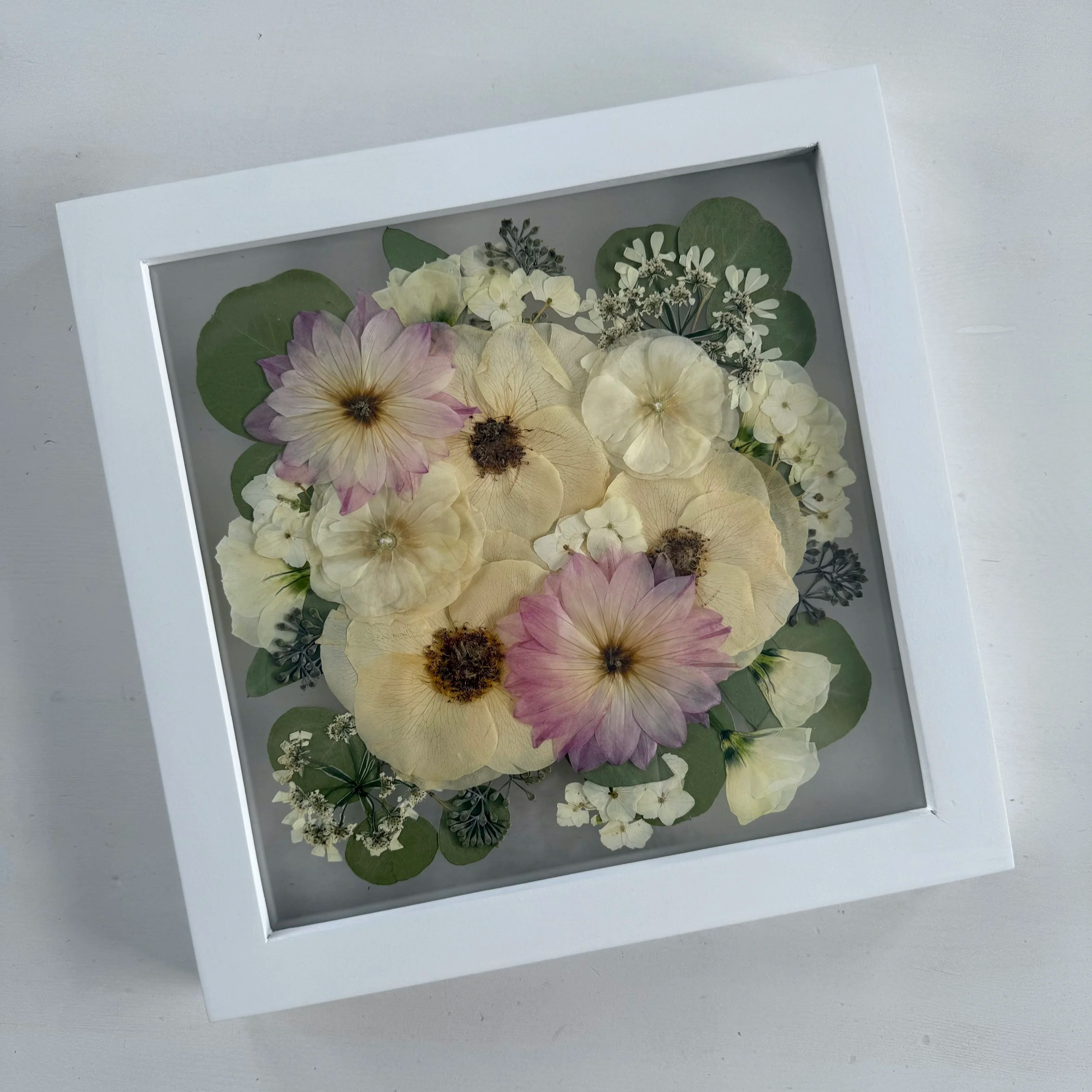 Framed pressed wedding bouquet flowers preserved in a floating glass frame.