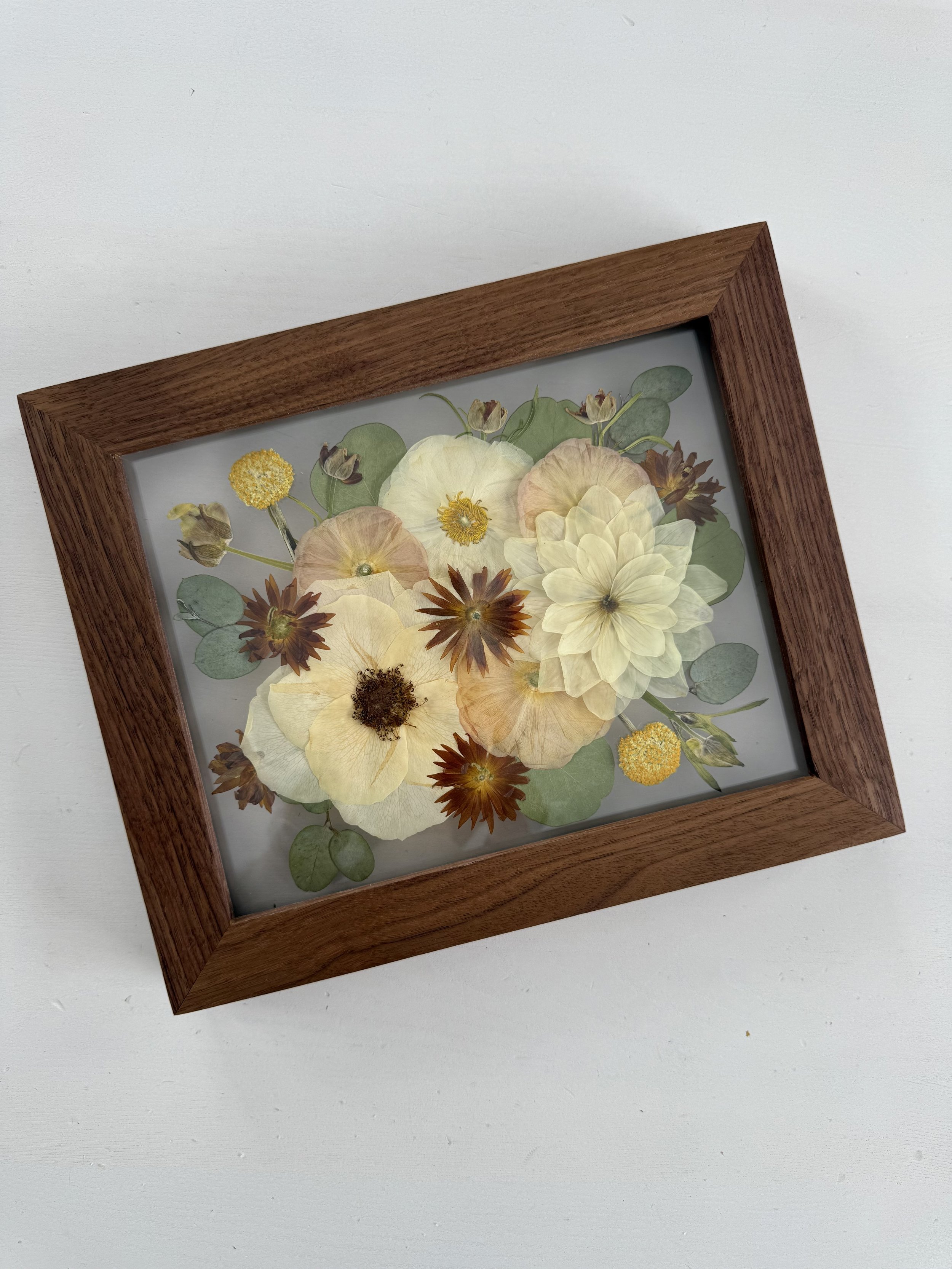 Framed pressed wedding bouquet flowers preserved in a floating glass frame.