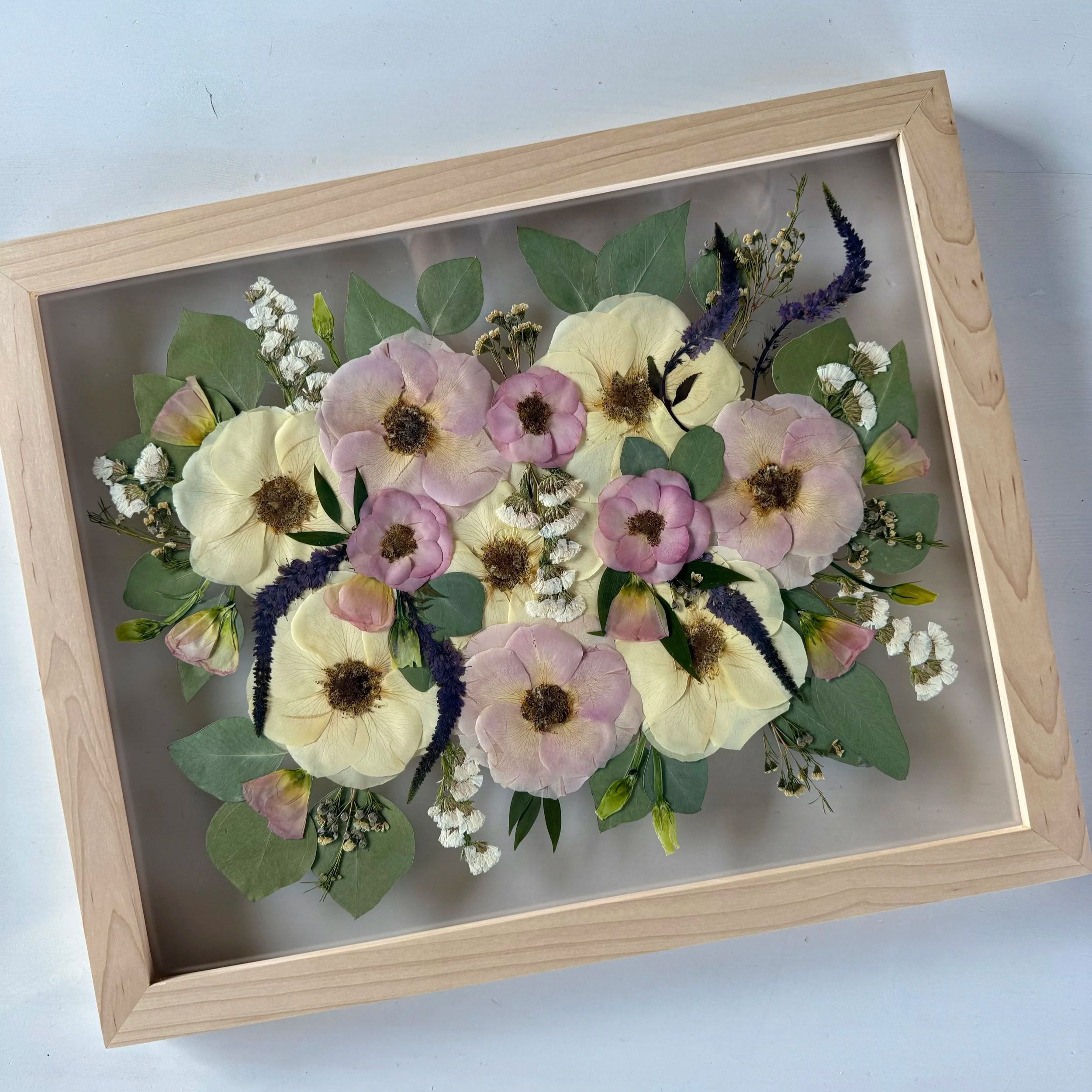 Framed pressed wedding bouquet flowers preserved in a floating glass frame.