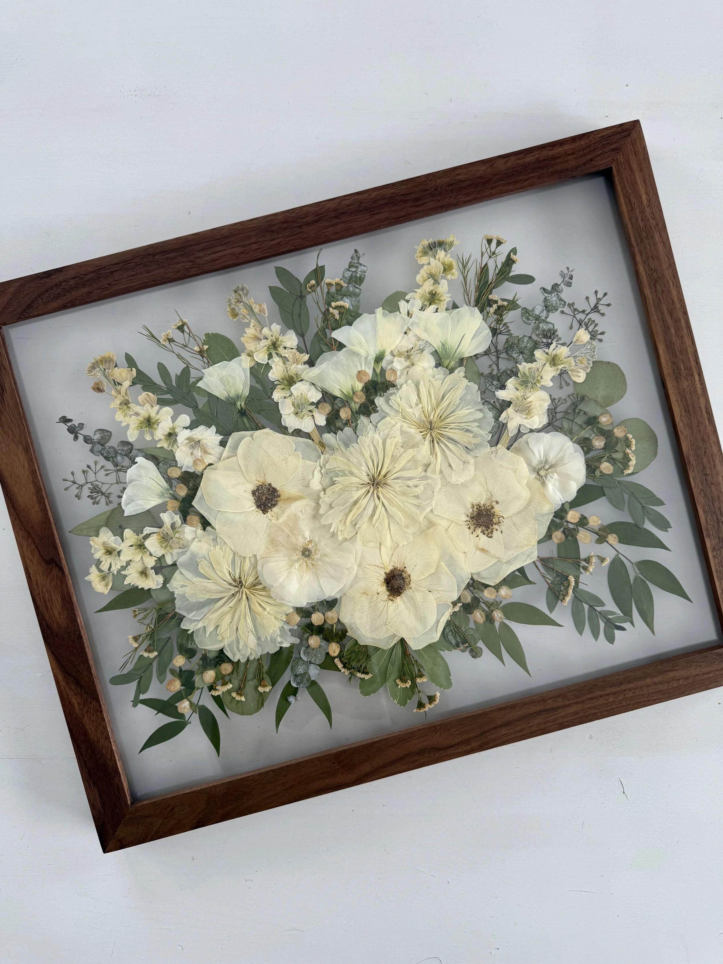 Framed pressed wedding bouquet flowers preserved in a floating glass frame.