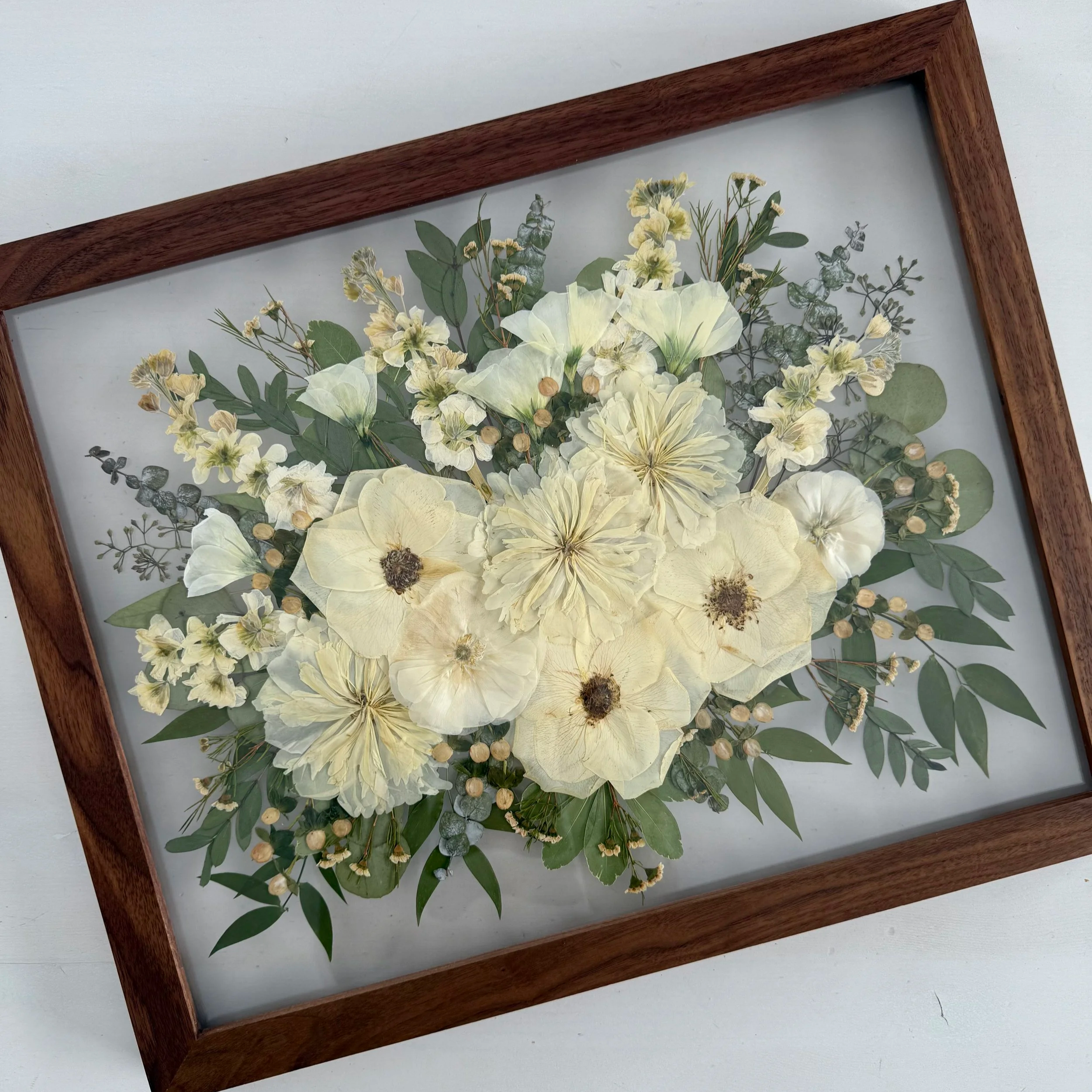Framed pressed wedding bouquet flowers preserved in a floating glass frame.