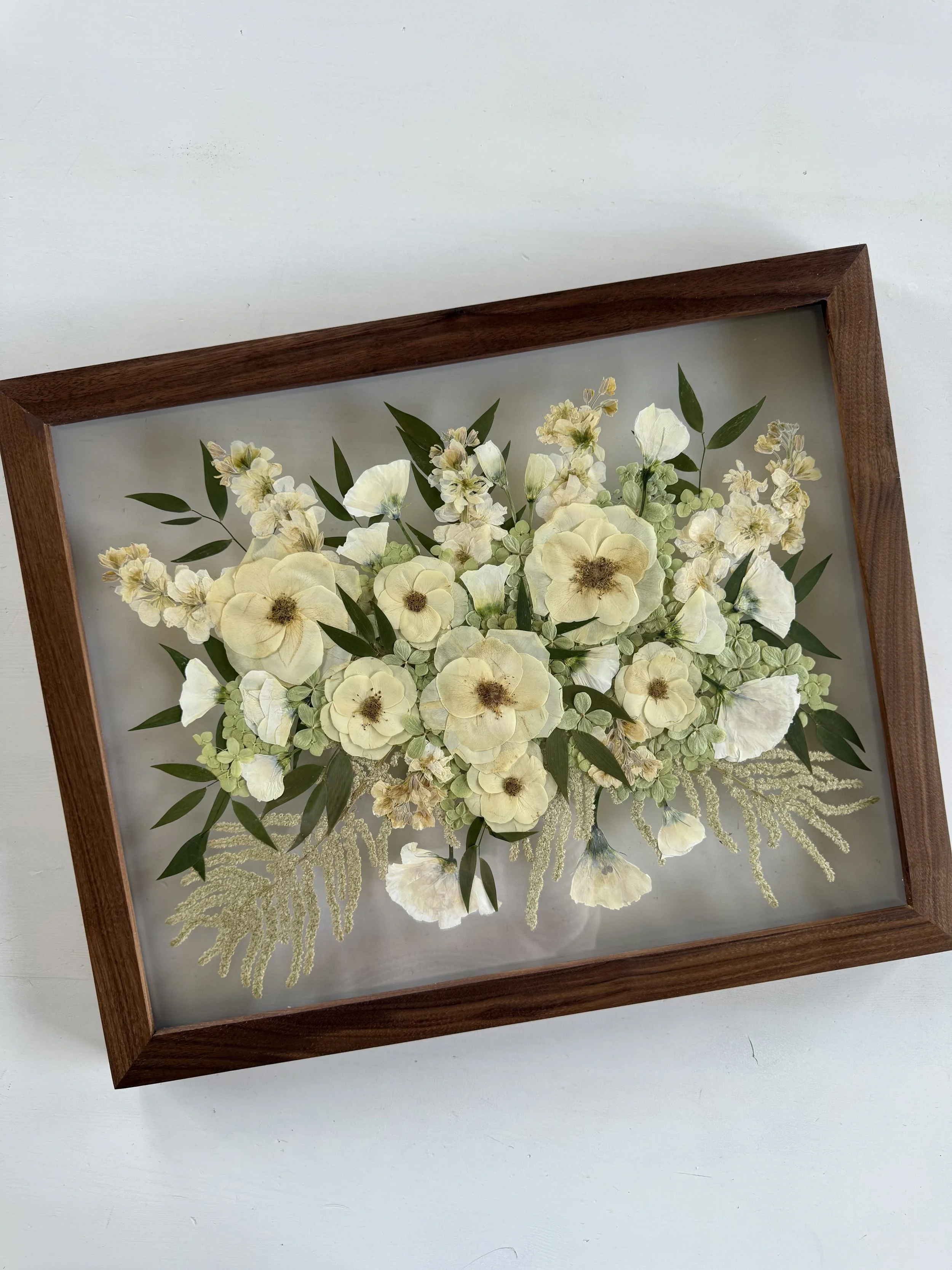 Framed pressed wedding bouquet flowers preserved in a floating glass frame.