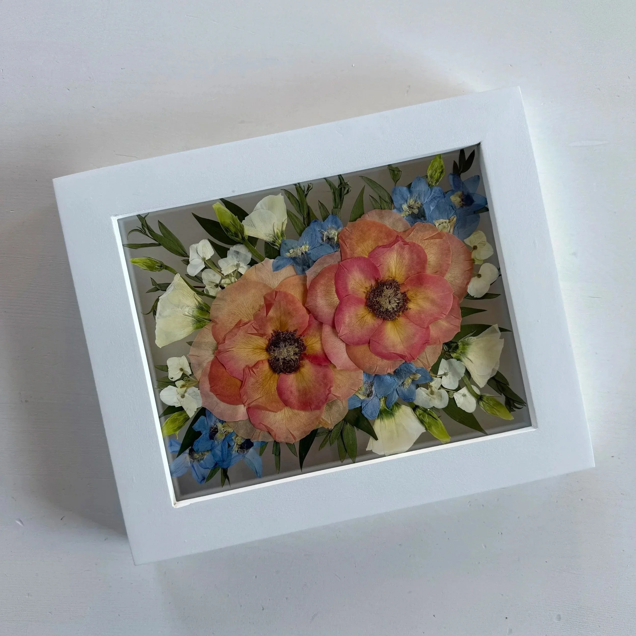 Framed pressed wedding bouquet flowers preserved in a floating glass frame.