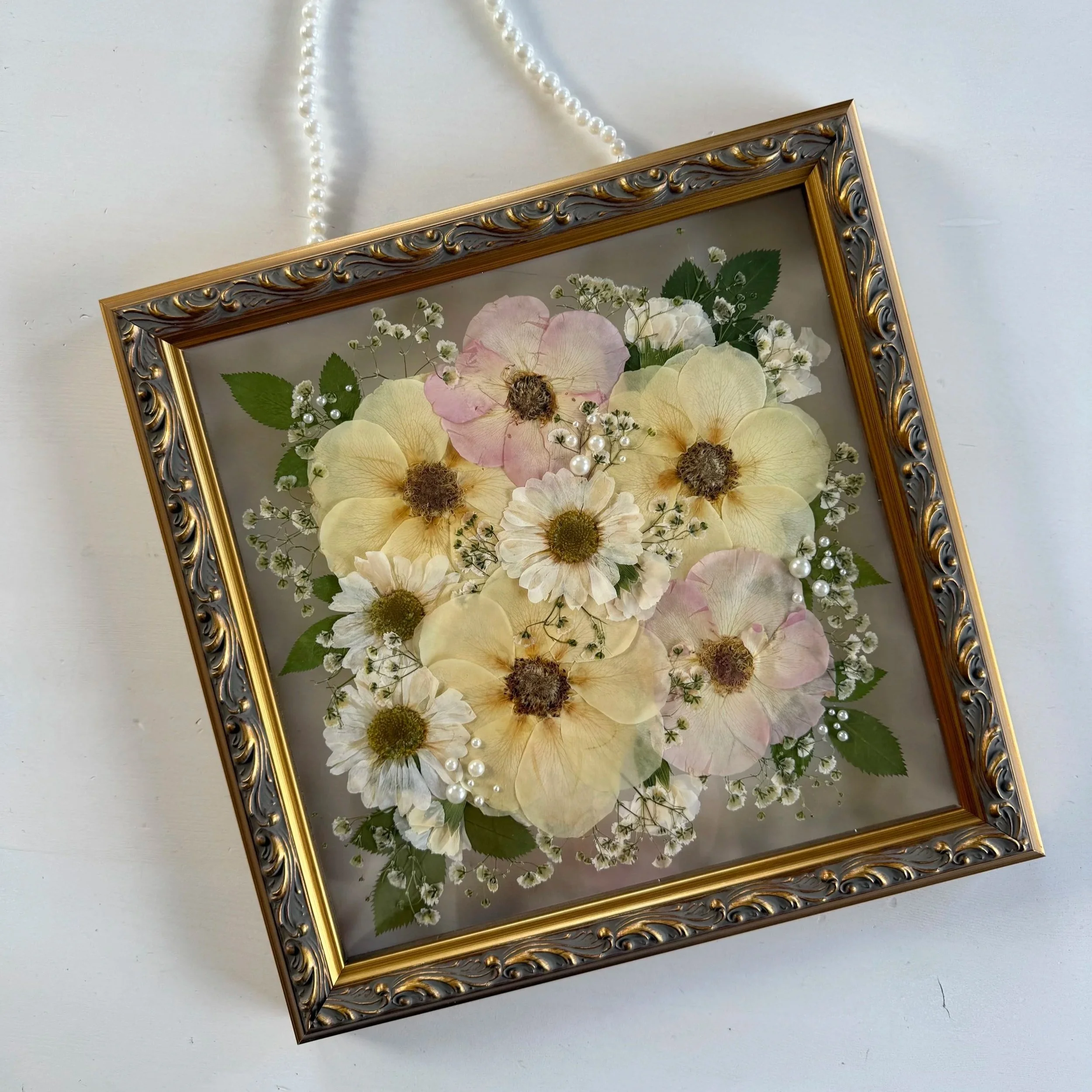 Framed pressed wedding bouquet flowers preserved in a floating glass frame.