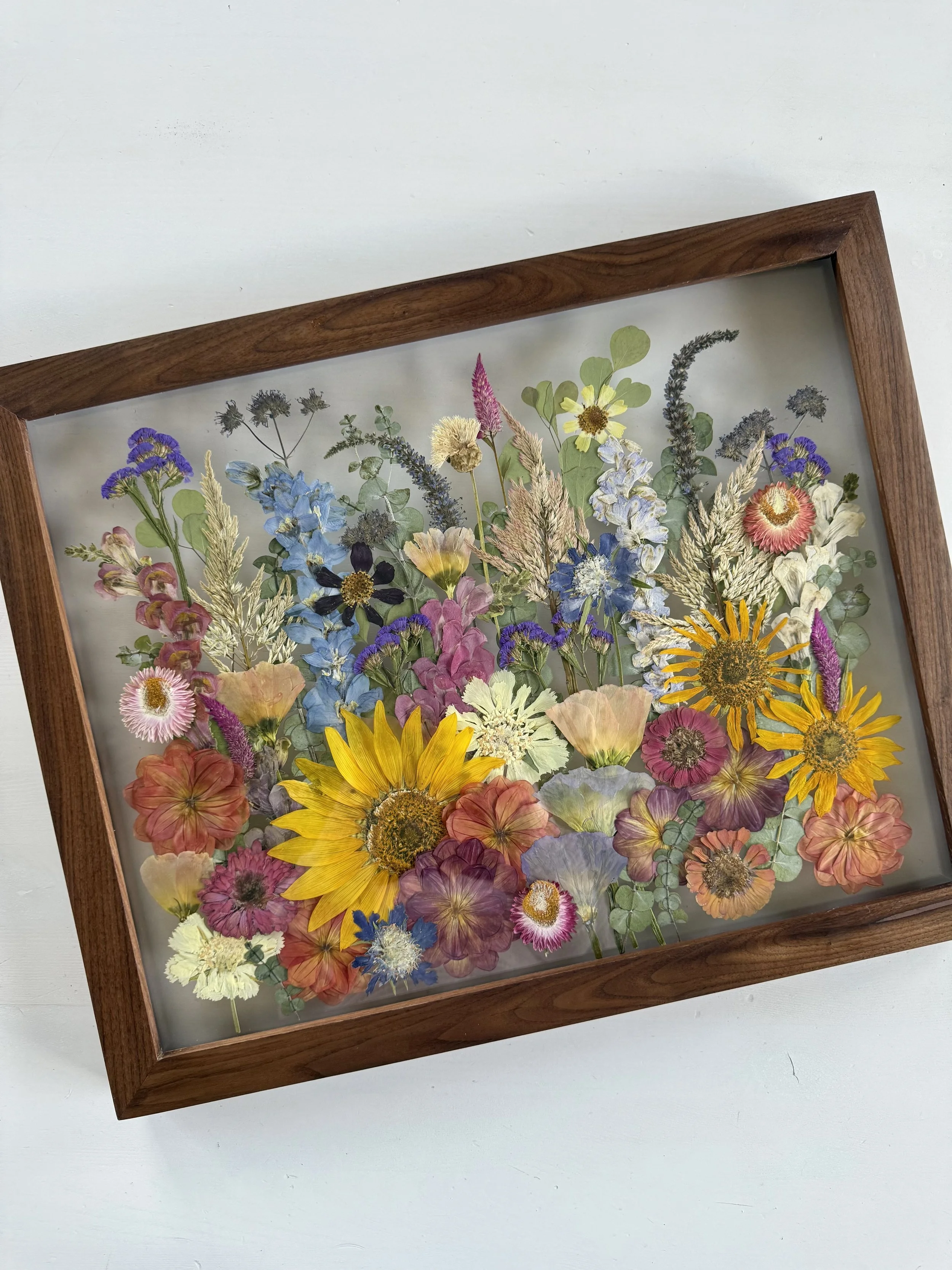Framed pressed wedding bouquet flowers preserved in a floating glass frame.