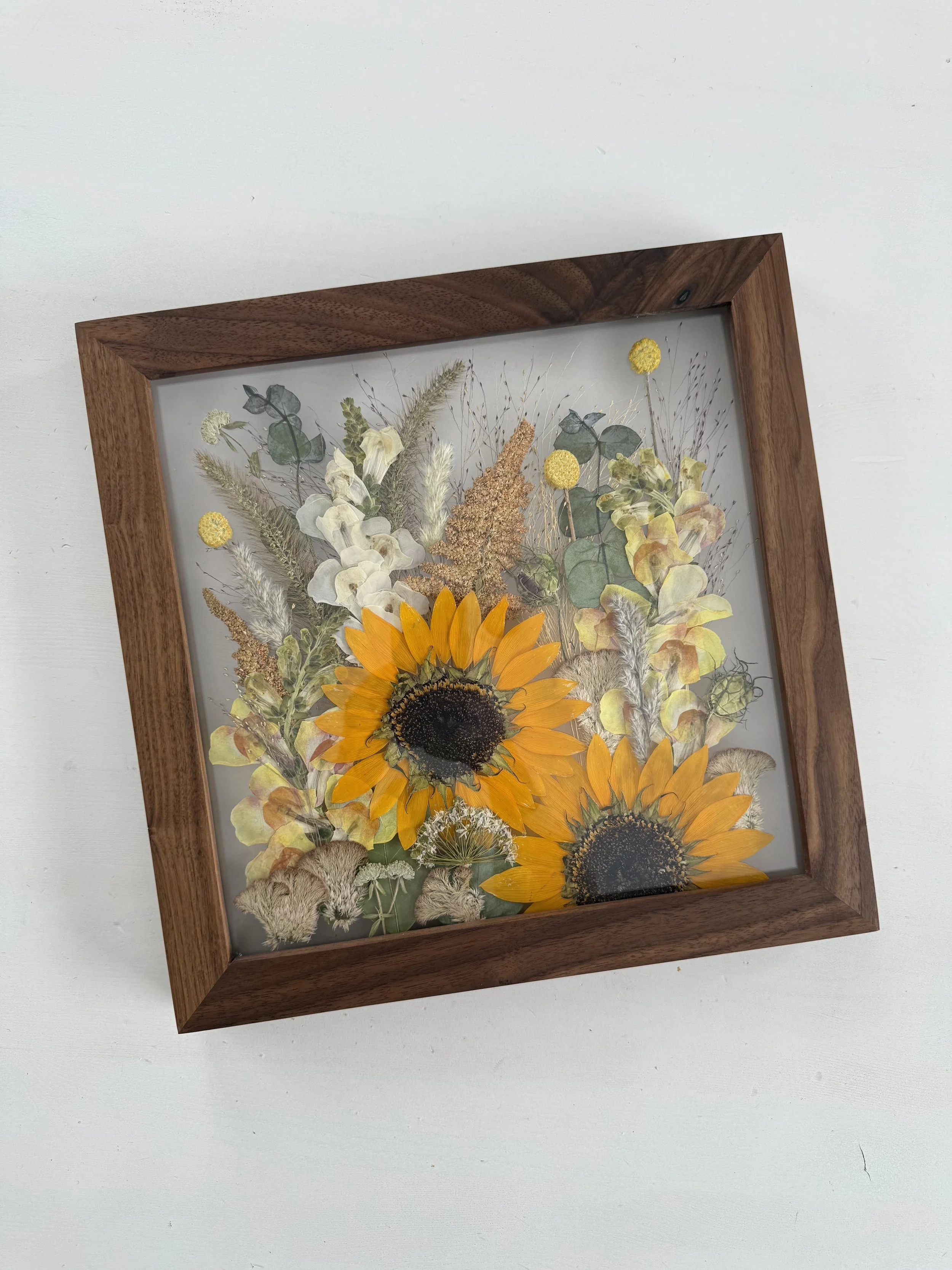 Framed pressed wedding bouquet flowers preserved in a floating glass frame.