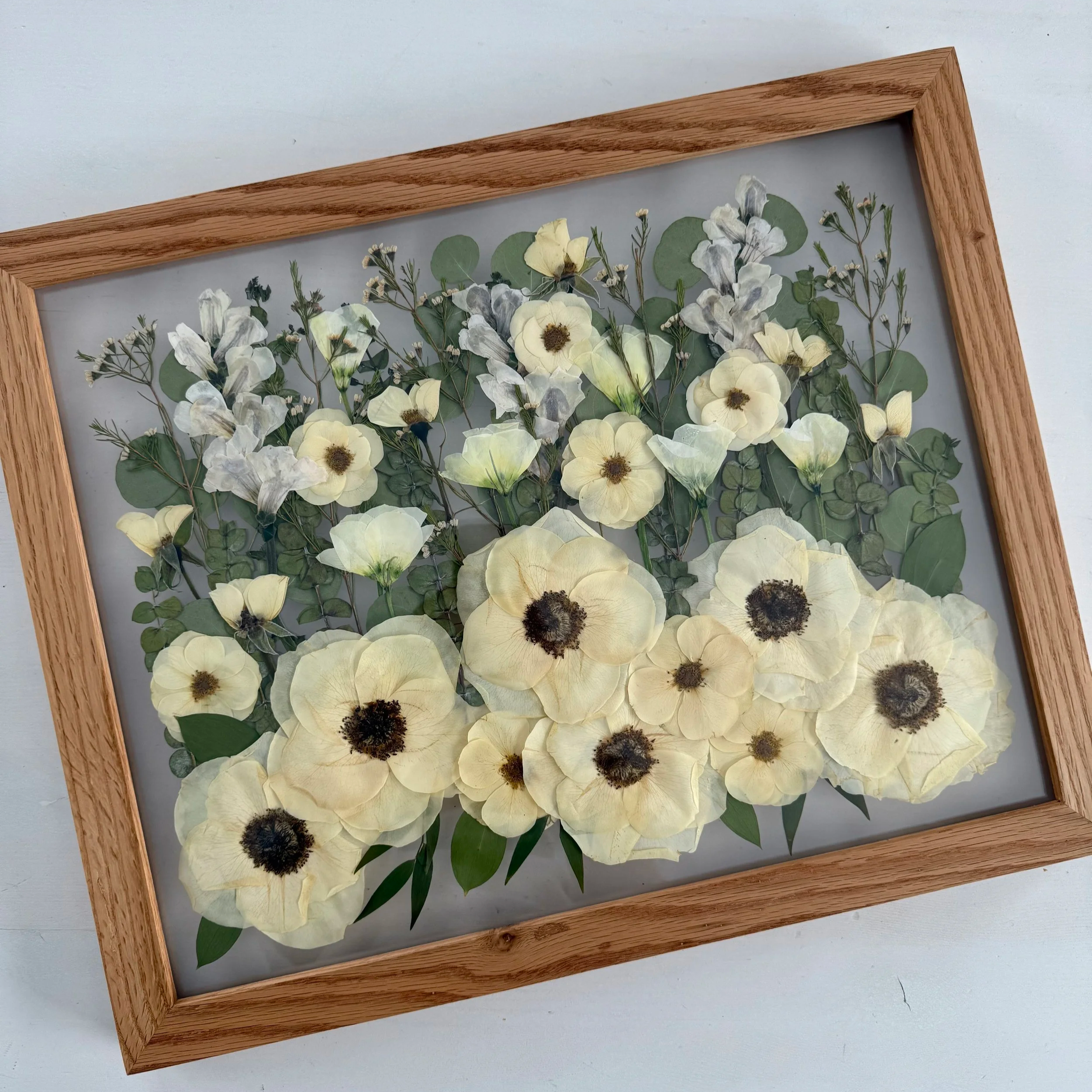 Framed pressed wedding bouquet flowers preserved in a floating glass frame.