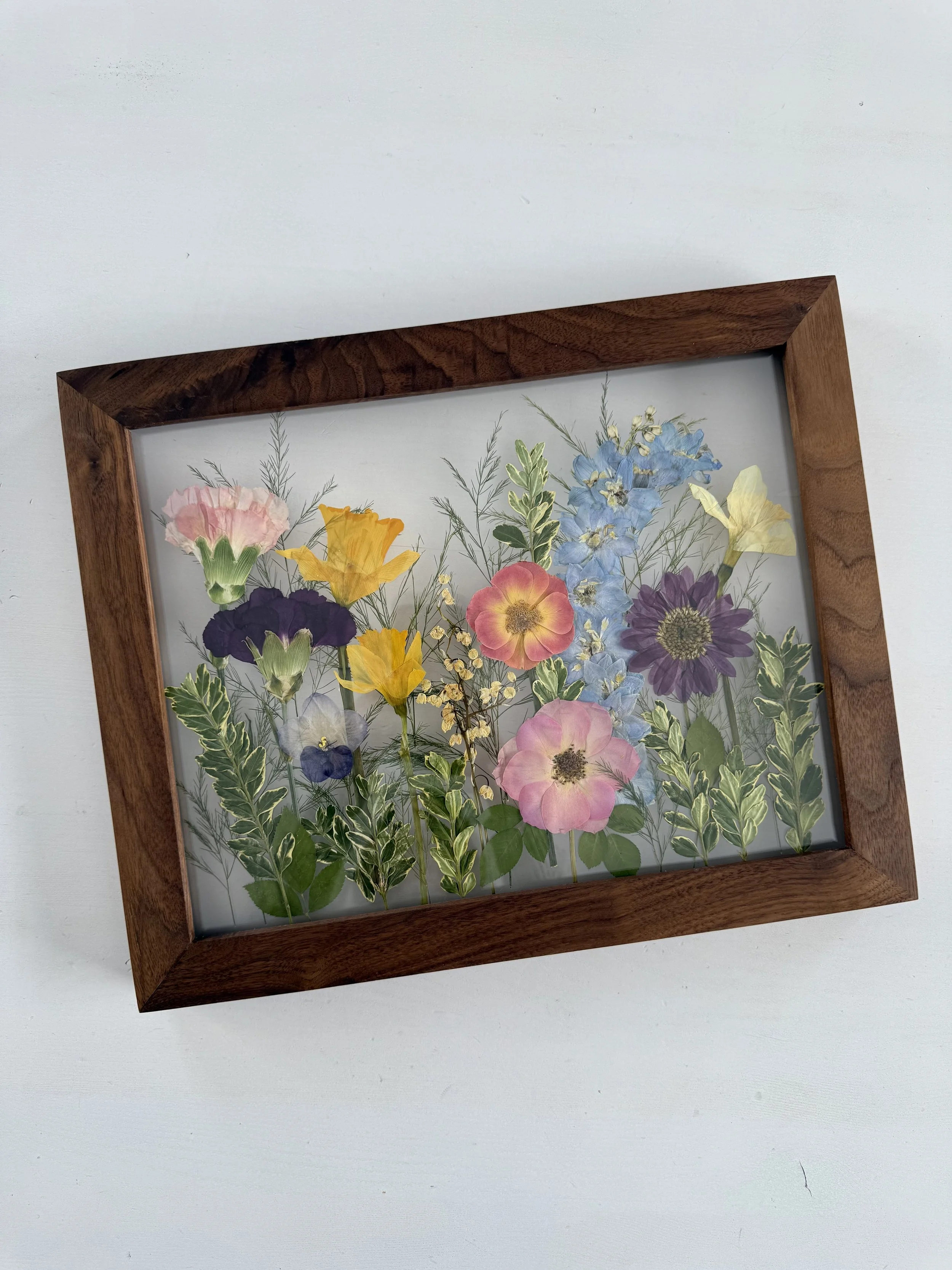 Framed pressed wedding bouquet flowers preserved in a floating glass frame.