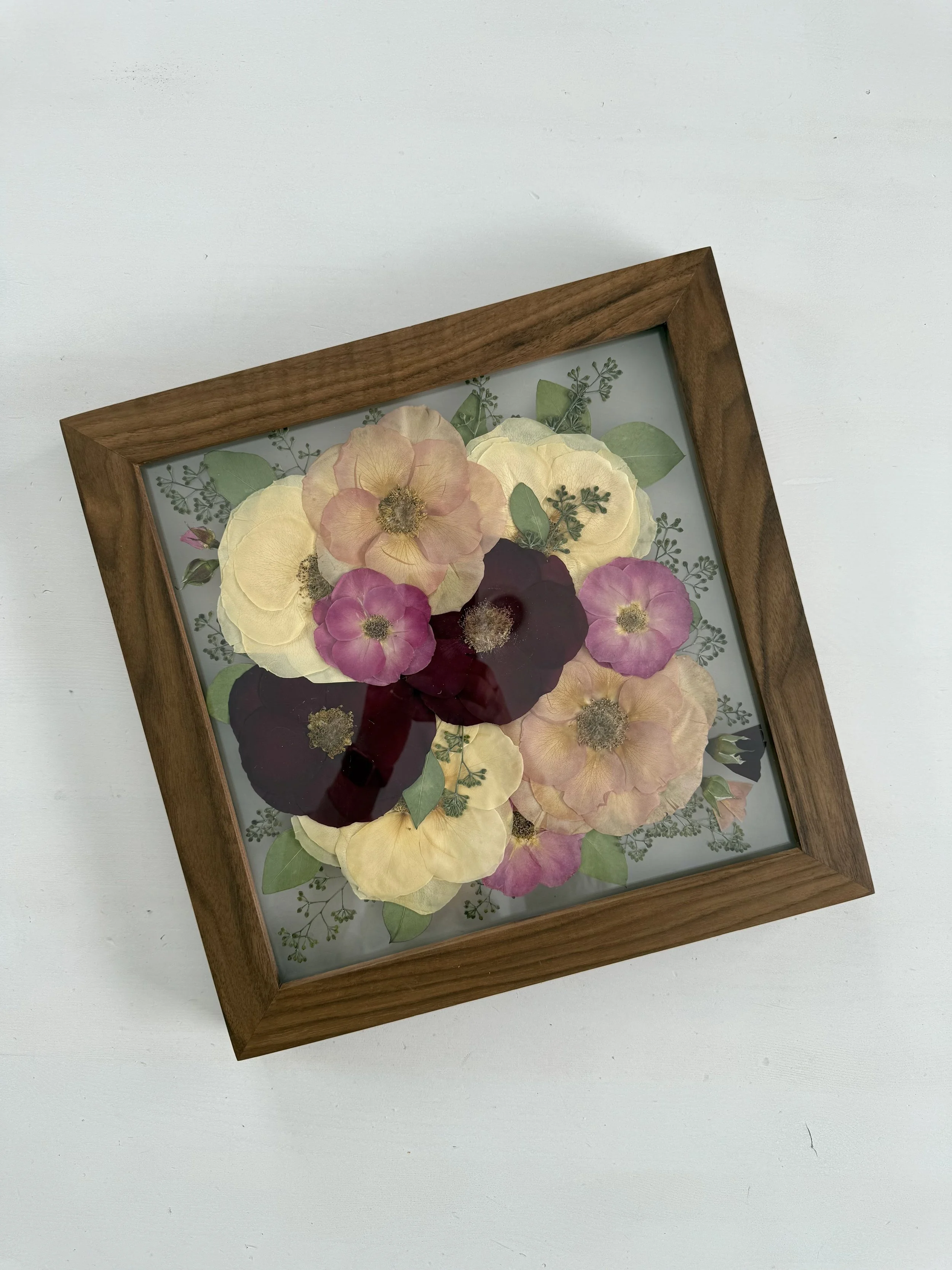Framed pressed wedding bouquet flowers preserved in a floating glass frame.