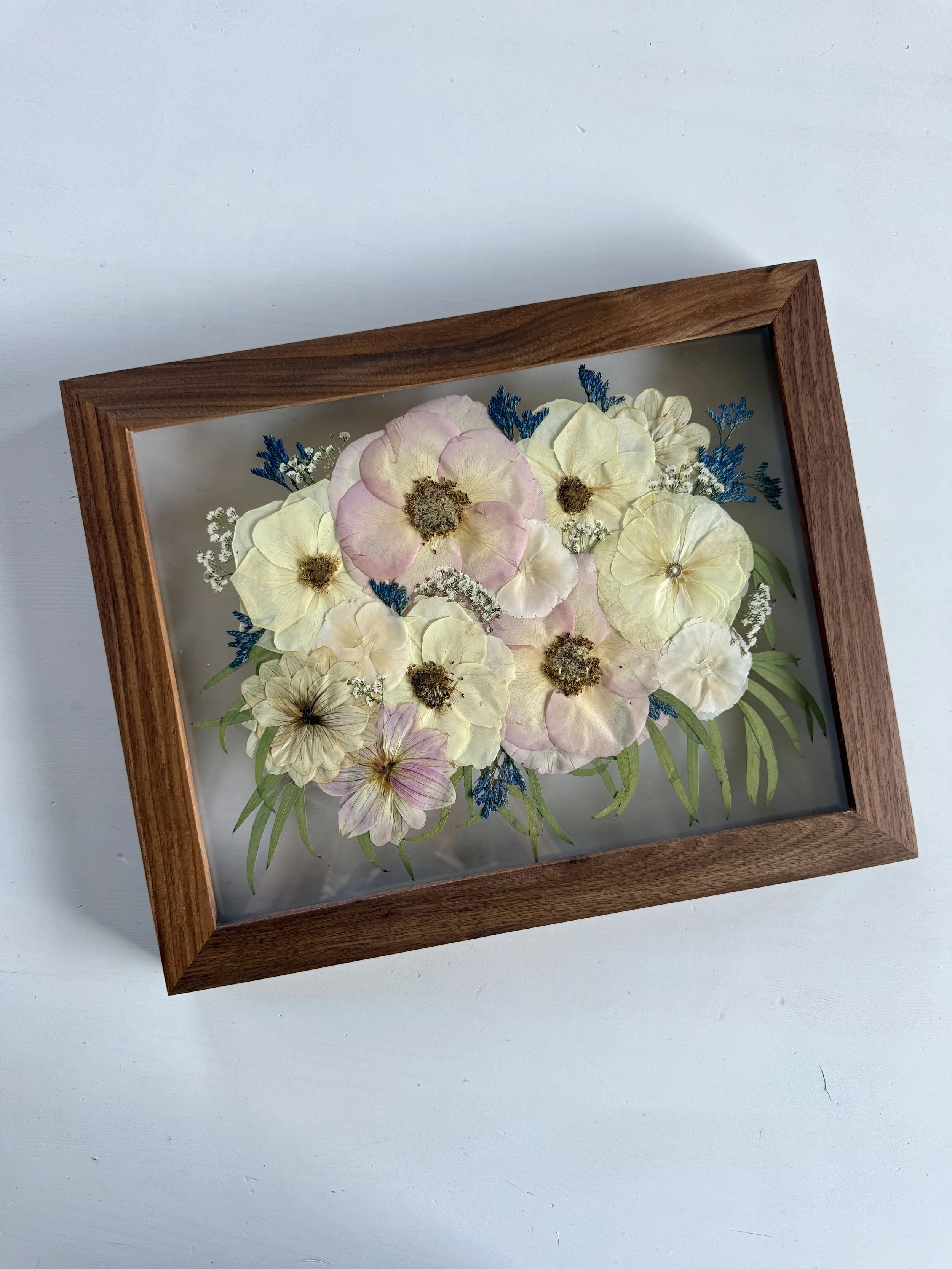 Framed pressed wedding bouquet flowers preserved in a floating glass frame.