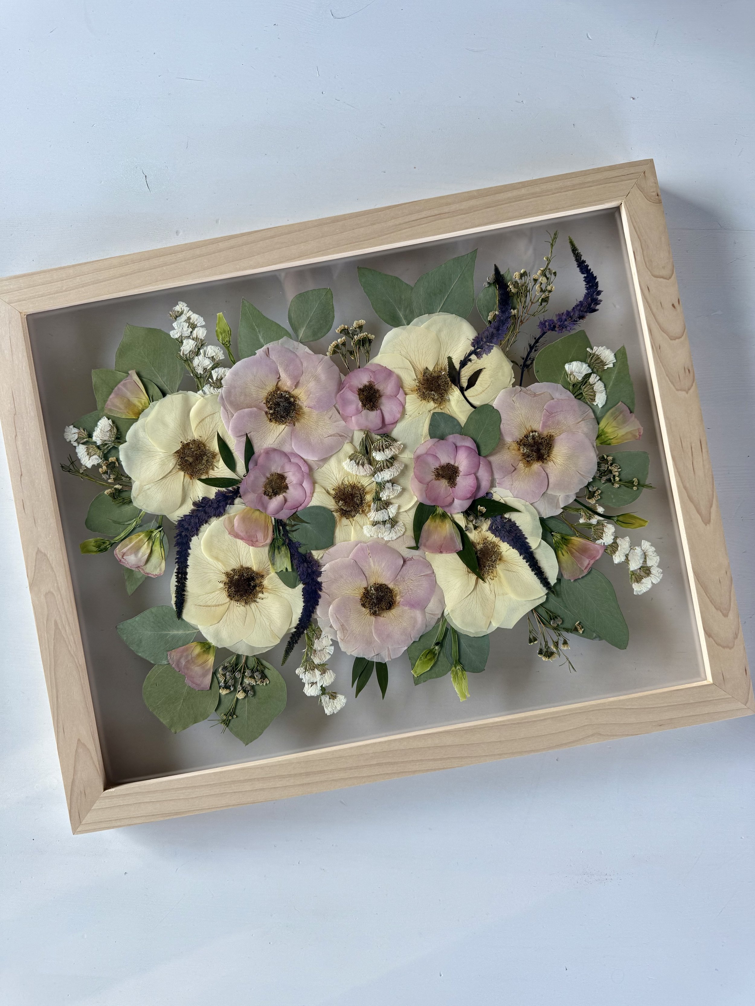 Framed pressed wedding bouquet flowers preserved in a floating glass frame.