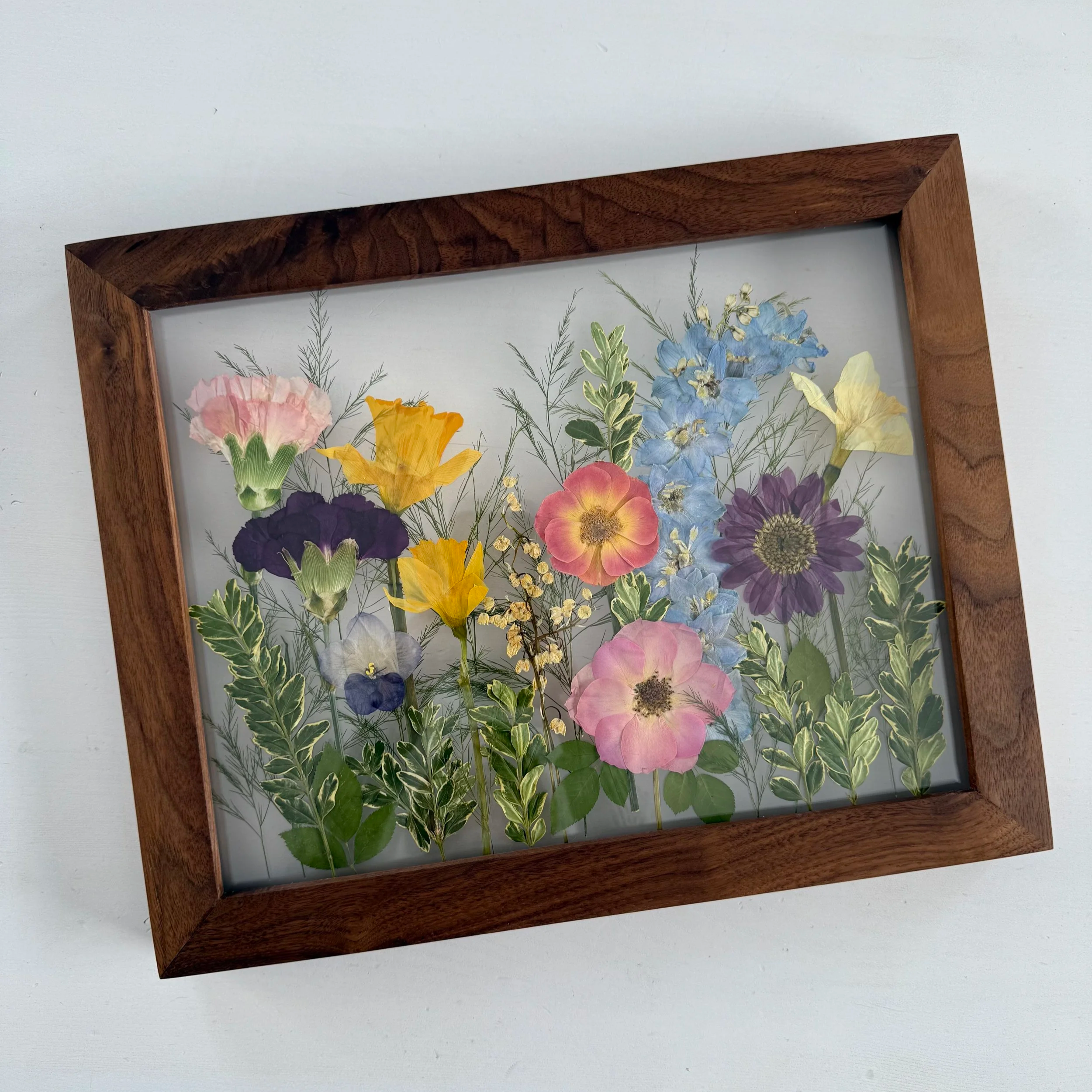 Framed pressed wedding bouquet flowers preserved in a floating glass frame.