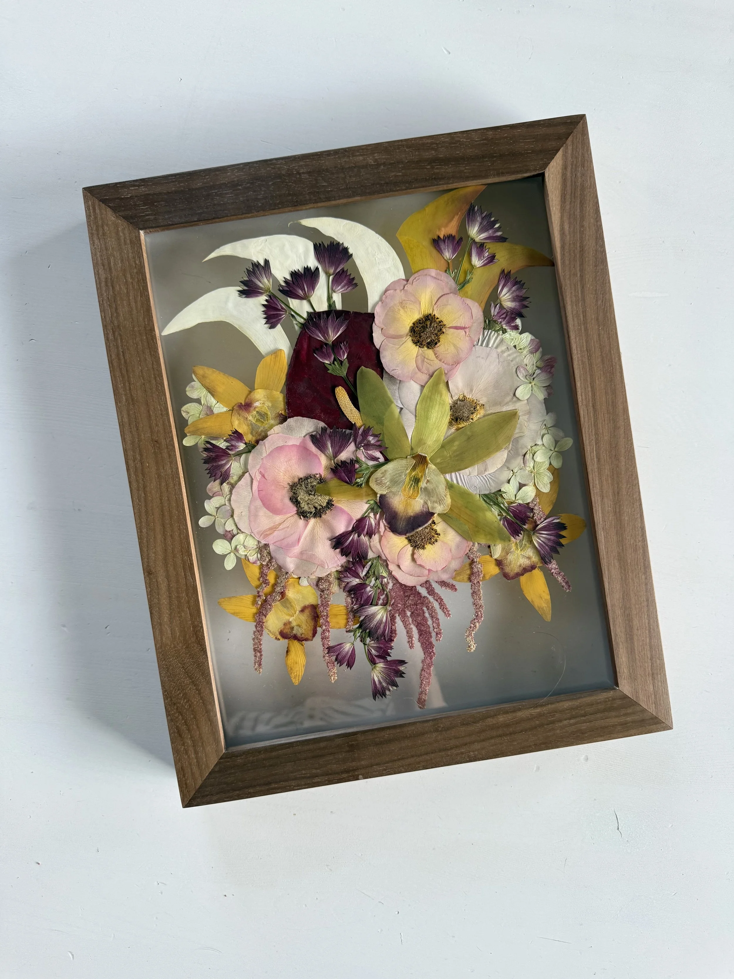Framed pressed wedding bouquet flowers preserved in a floating glass frame.