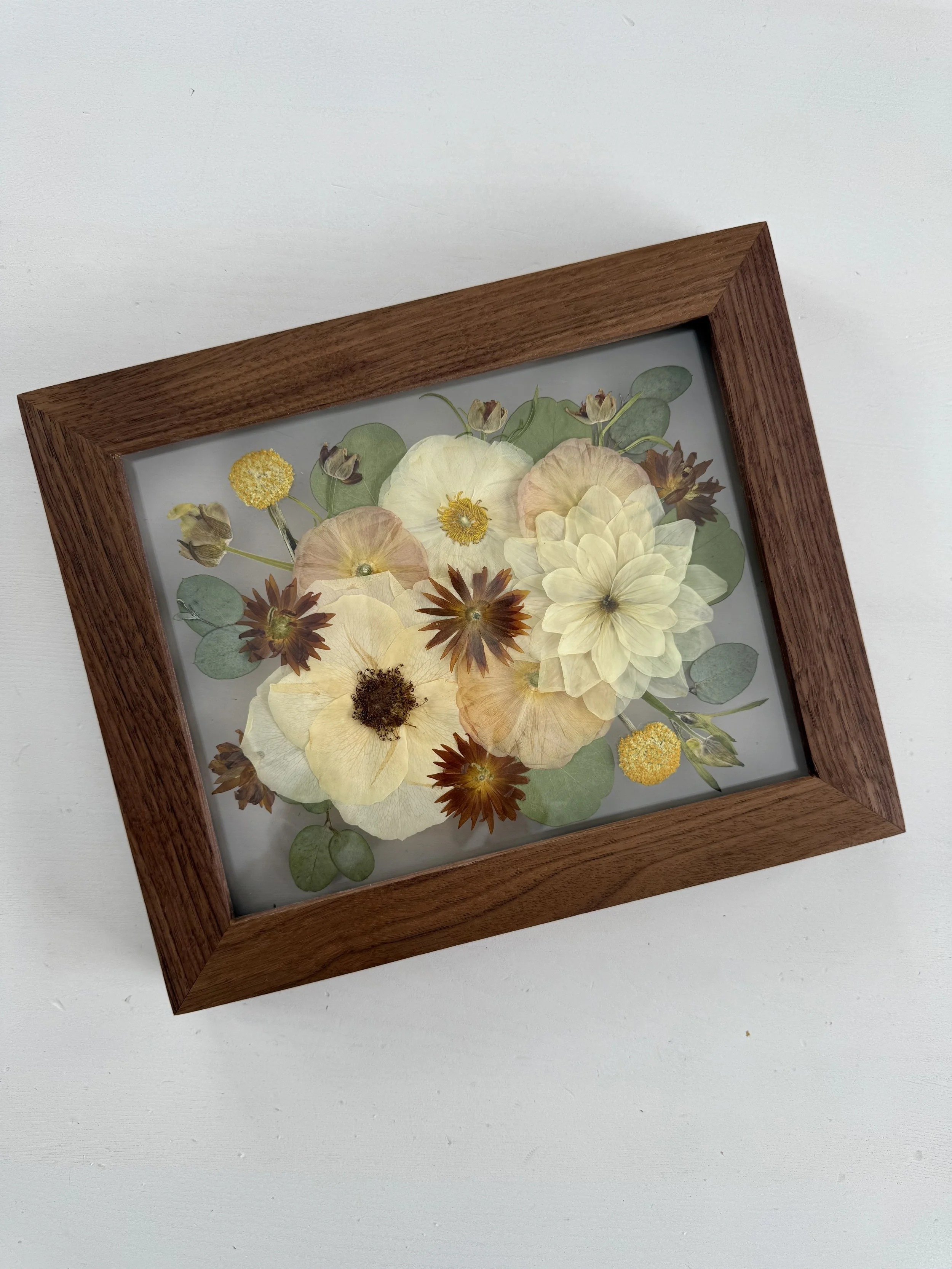 Framed pressed wedding bouquet flowers preserved in a floating glass frame.