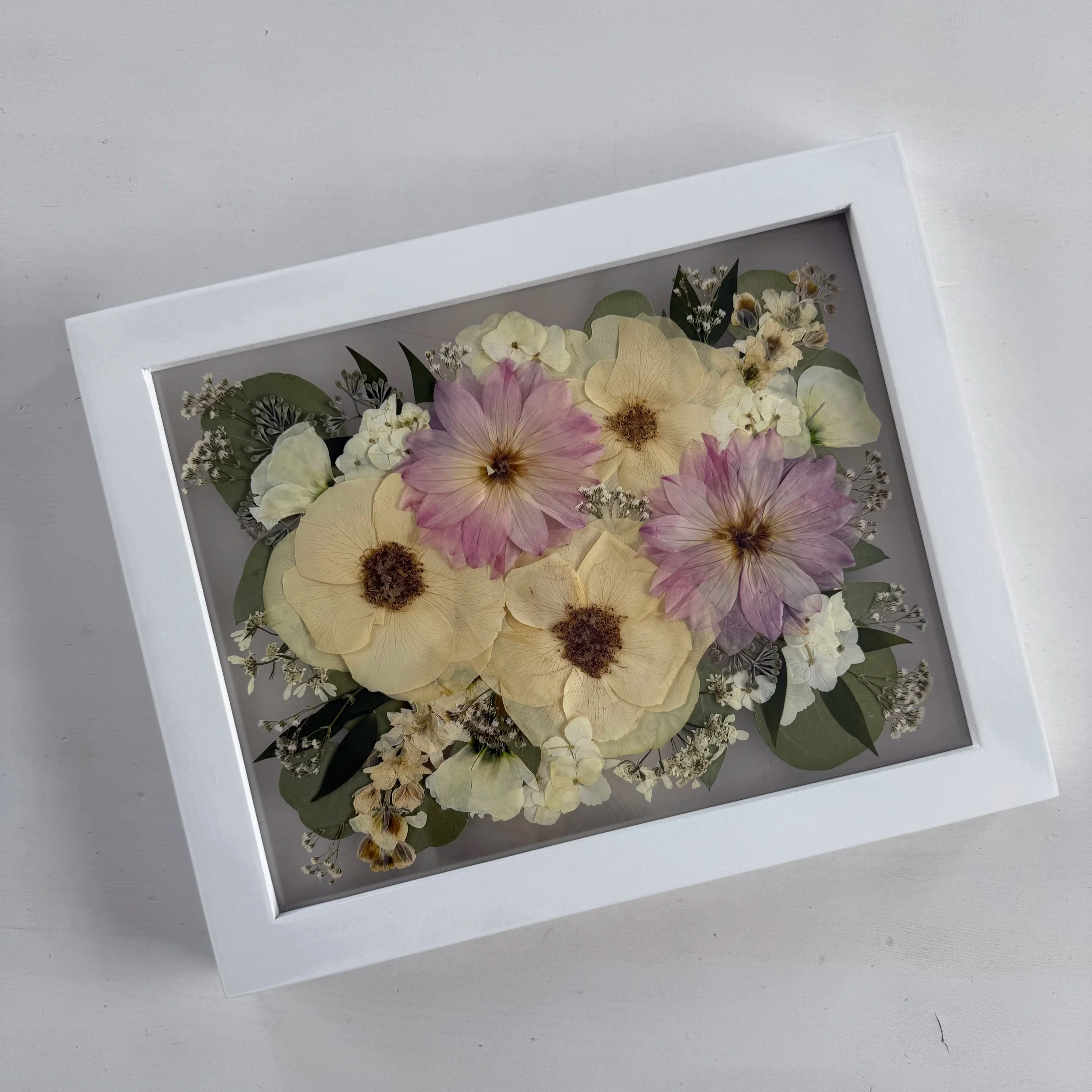 Framed pressed wedding bouquet flowers preserved in a floating glass frame.
