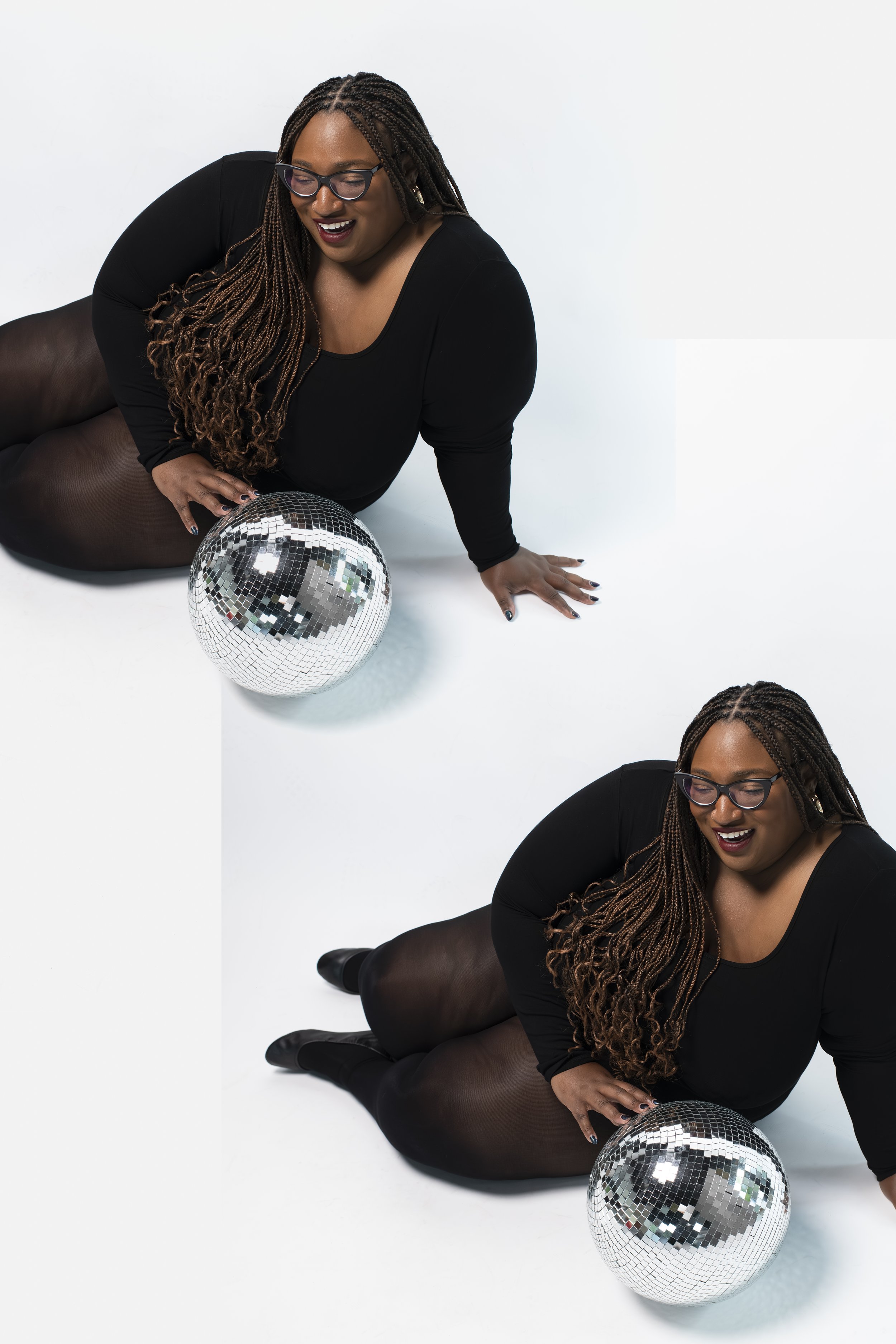 A woman with glasses and long braided hair, wearing a black top and sheer black tights, is sitting on the floor with a disco ball in front of her, smiling and looking down.