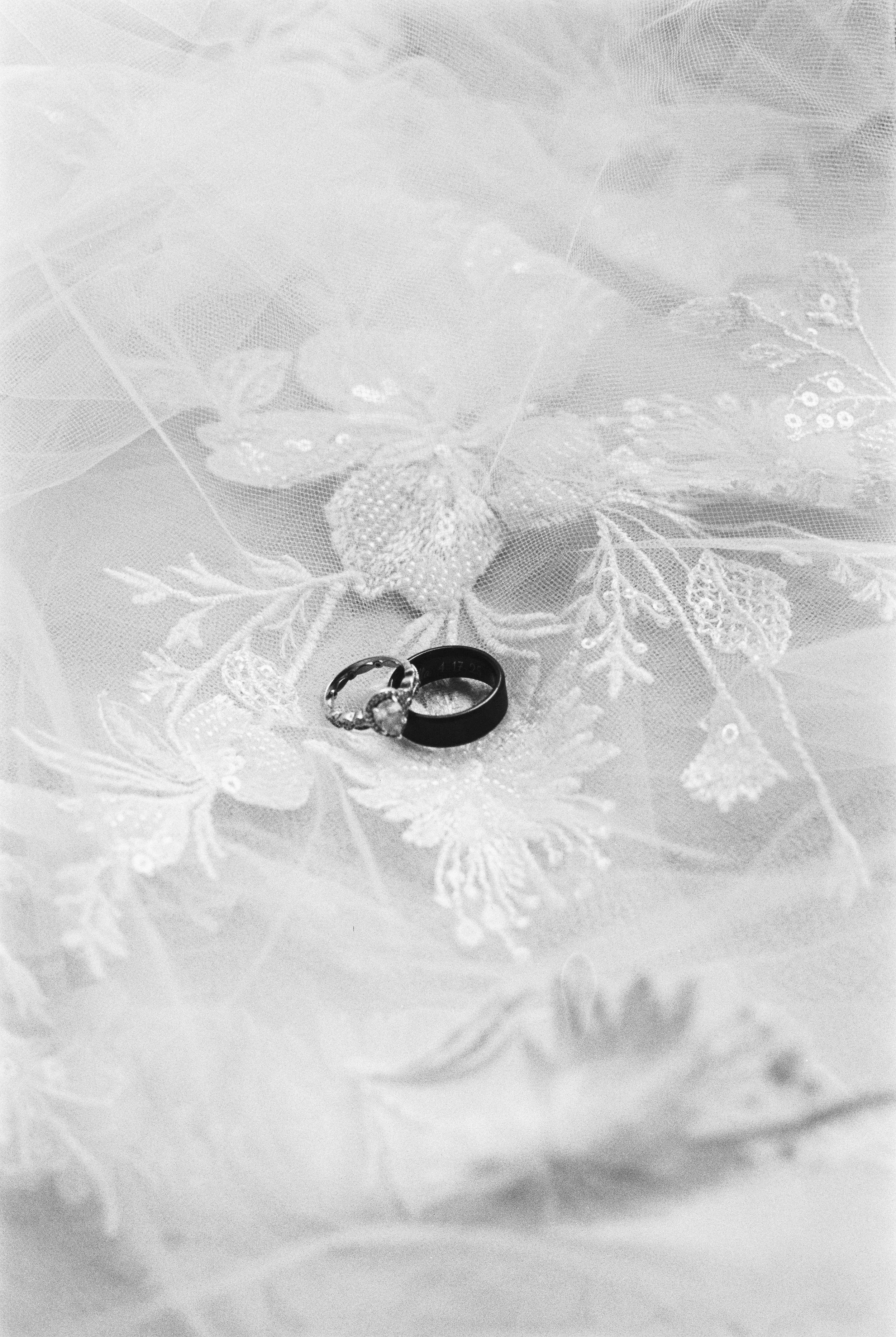 Black wedding rings placed on a lace fabric with floral embroidery.