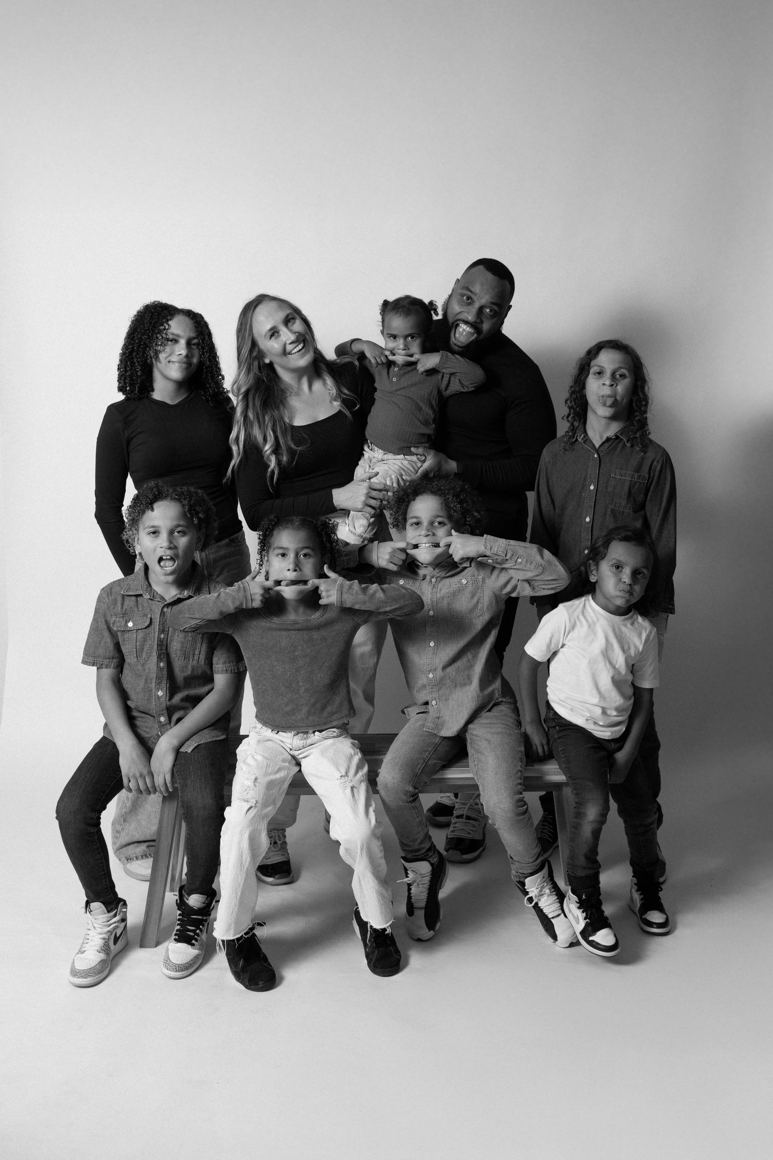 A black and white photo of a family group posing together, with adults and children making playful faces and gestures.