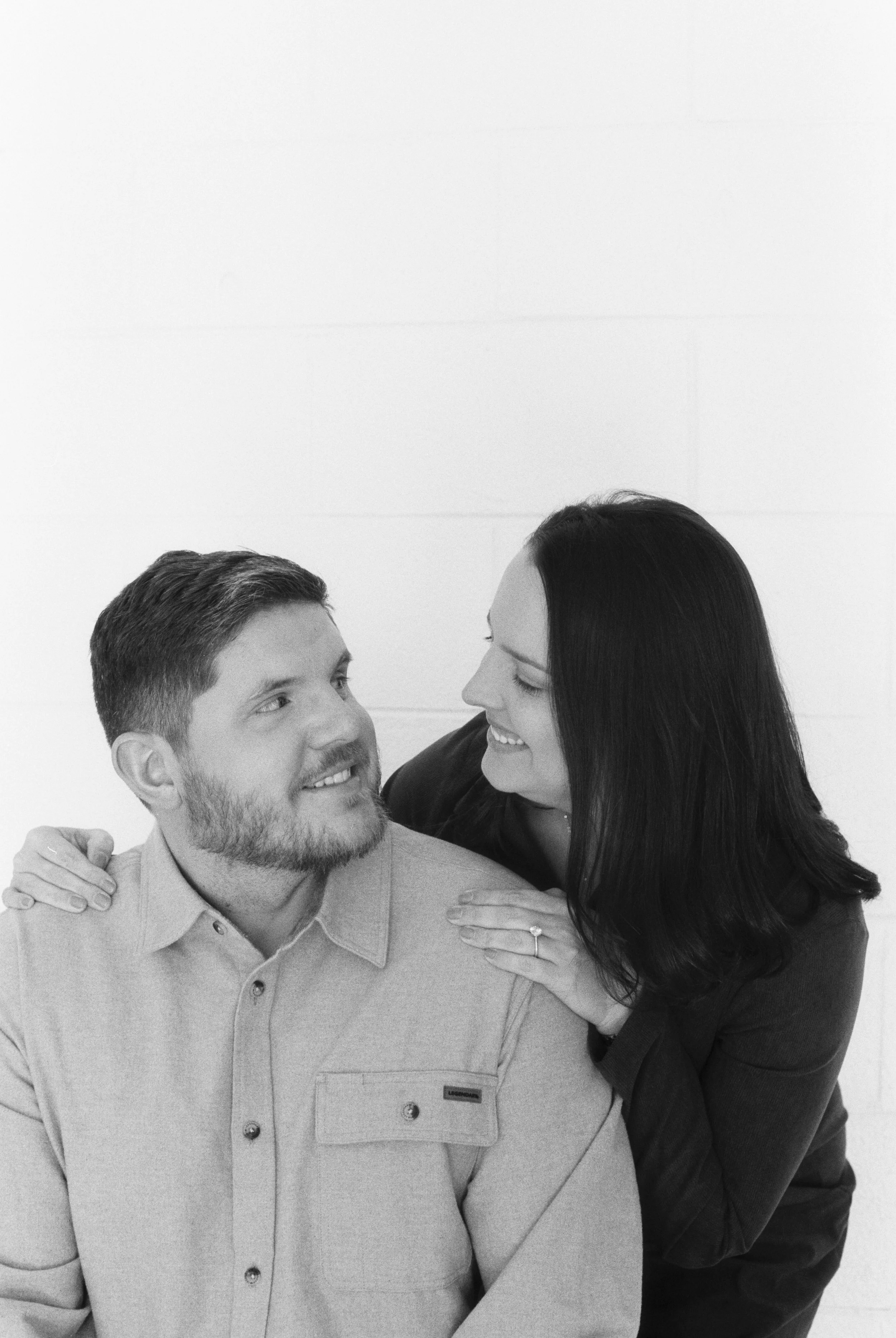 A smiling woman with long dark hair embraces a man with a beard, looking at each other affectionately.