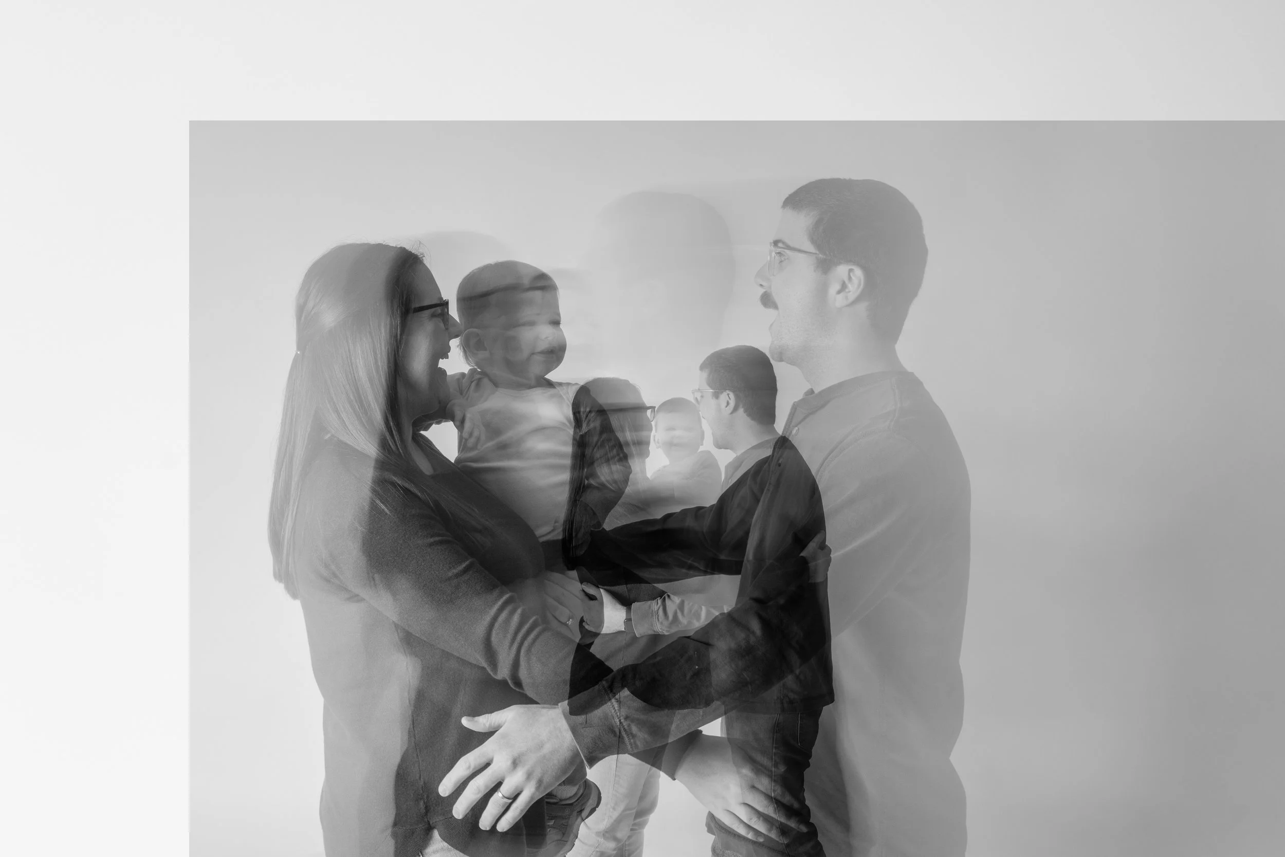 Black and white photo of a smiling woman holding a young girl, with a man facing them, all appearing as layered, overlapping images.