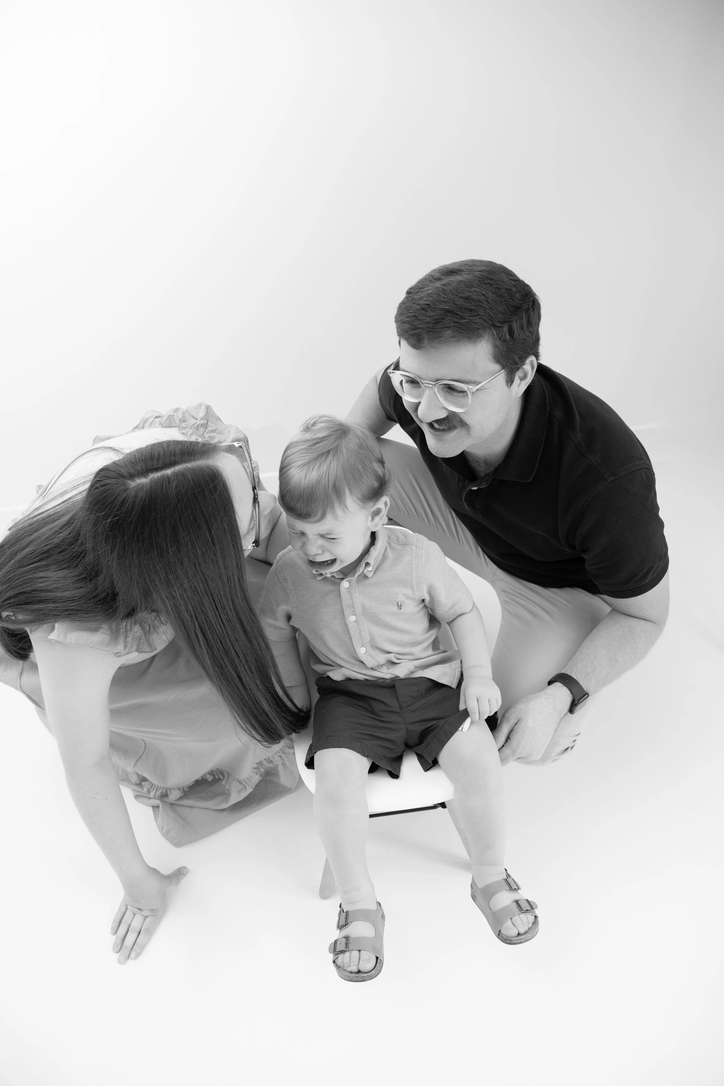 A family with a mother, father, and young son sitting together. The boy appears to be upset or crying, while the parents are leaning in to comfort him.