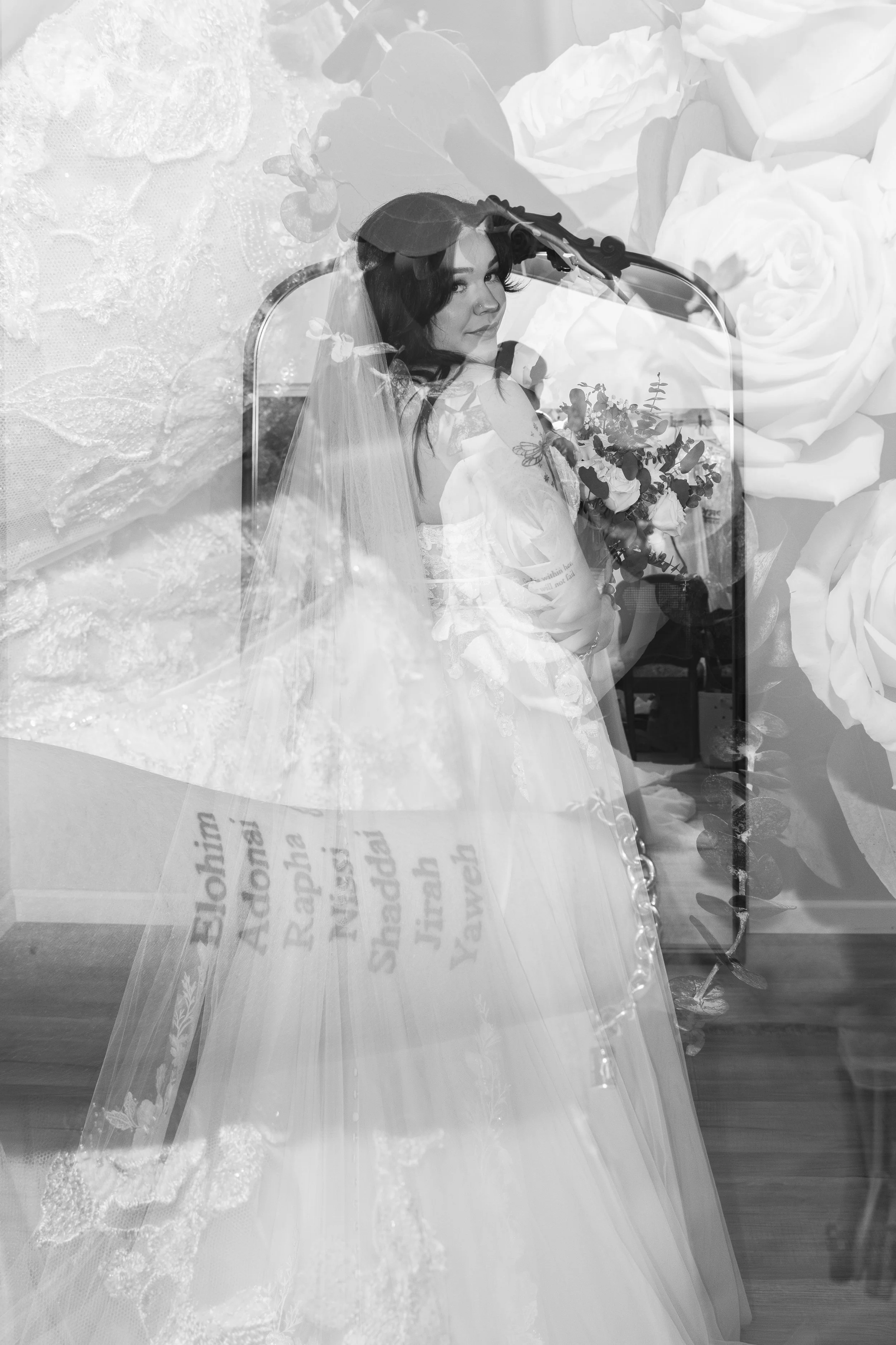 A woman in a wedding dress and veil holding a bouquet, seen through a mirror with a floral background.