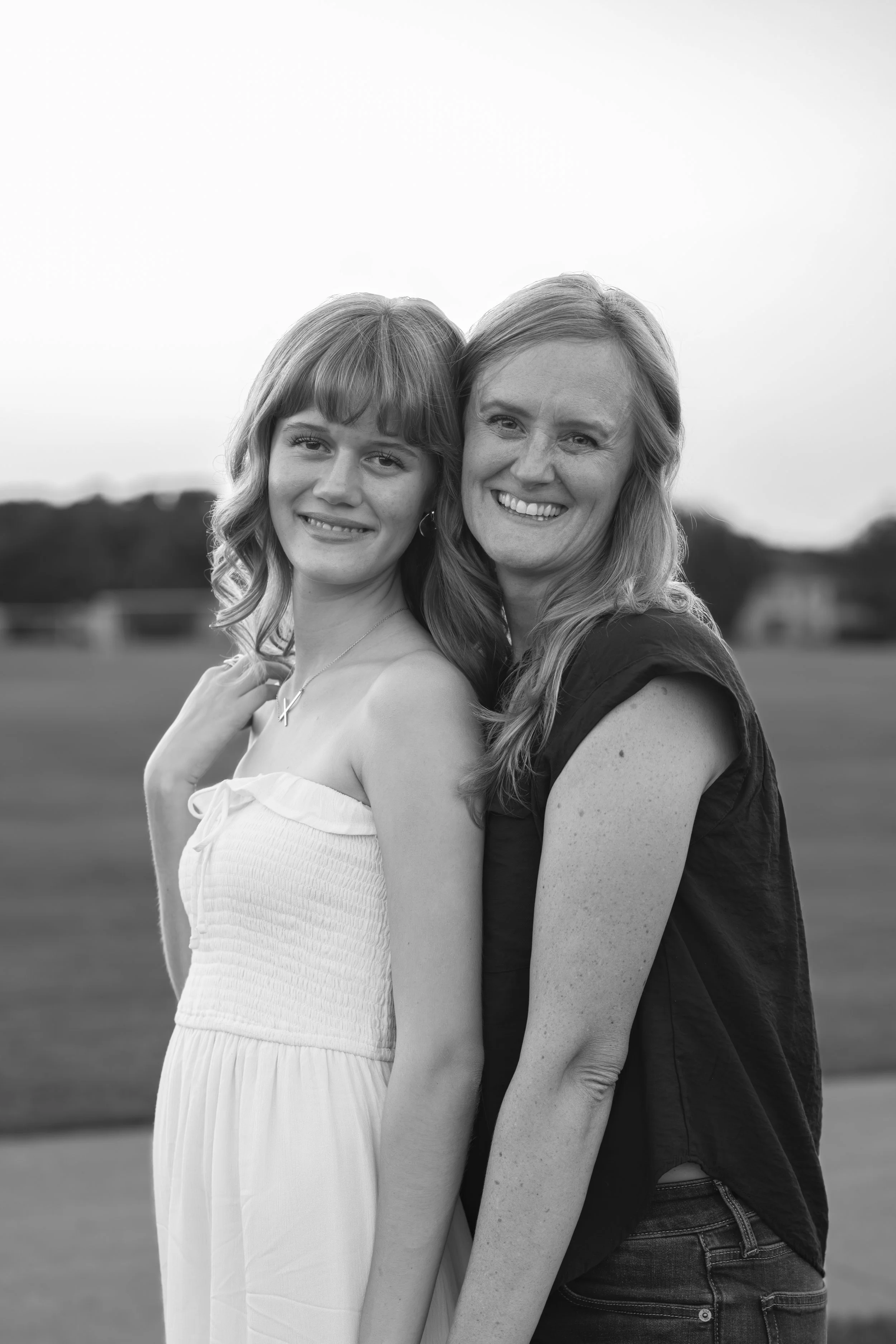 Black and white photo of a young woman and an older woman standing close together outdoors, smiling.