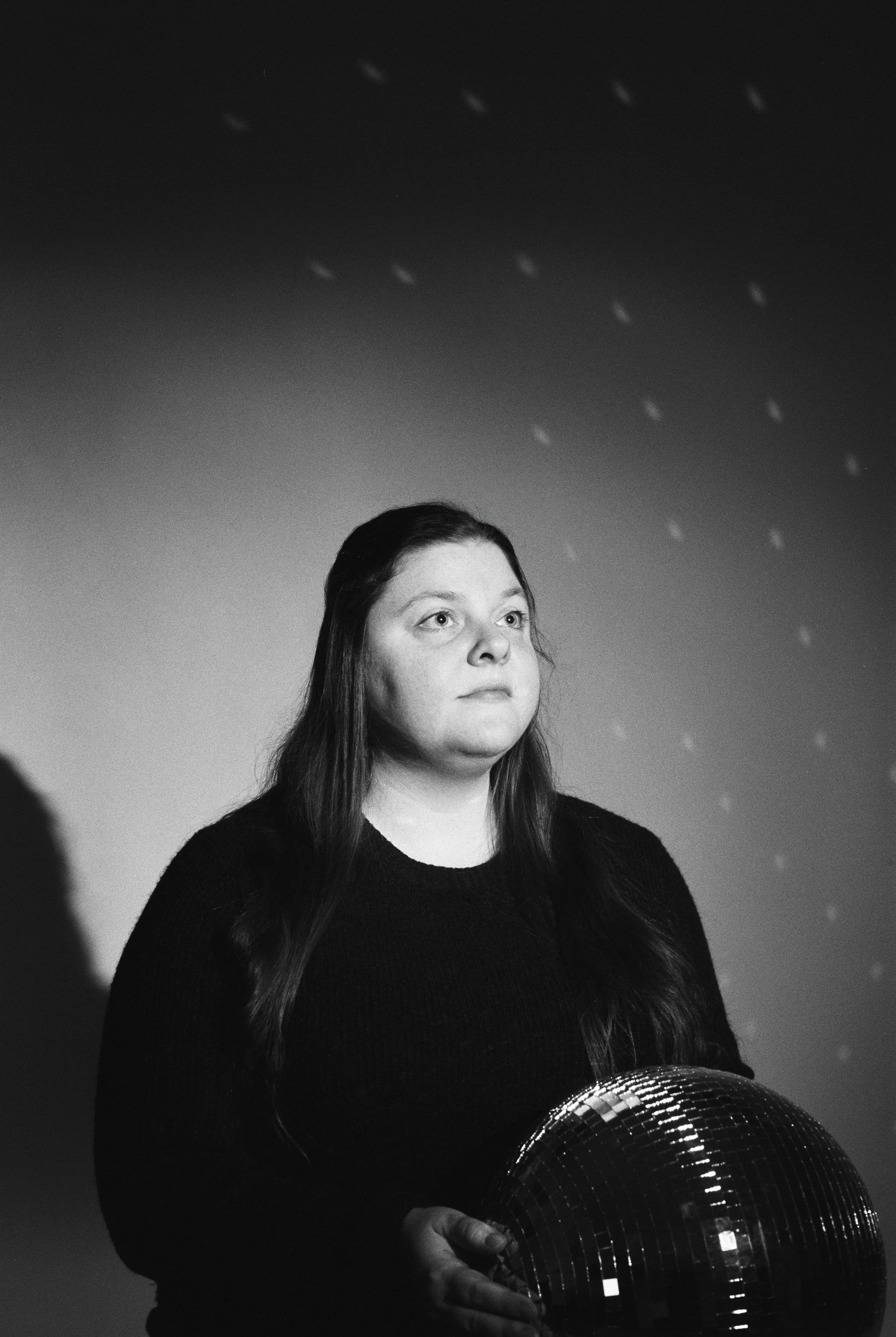 A woman with long hair holding a disco ball in a room, black and white photo.