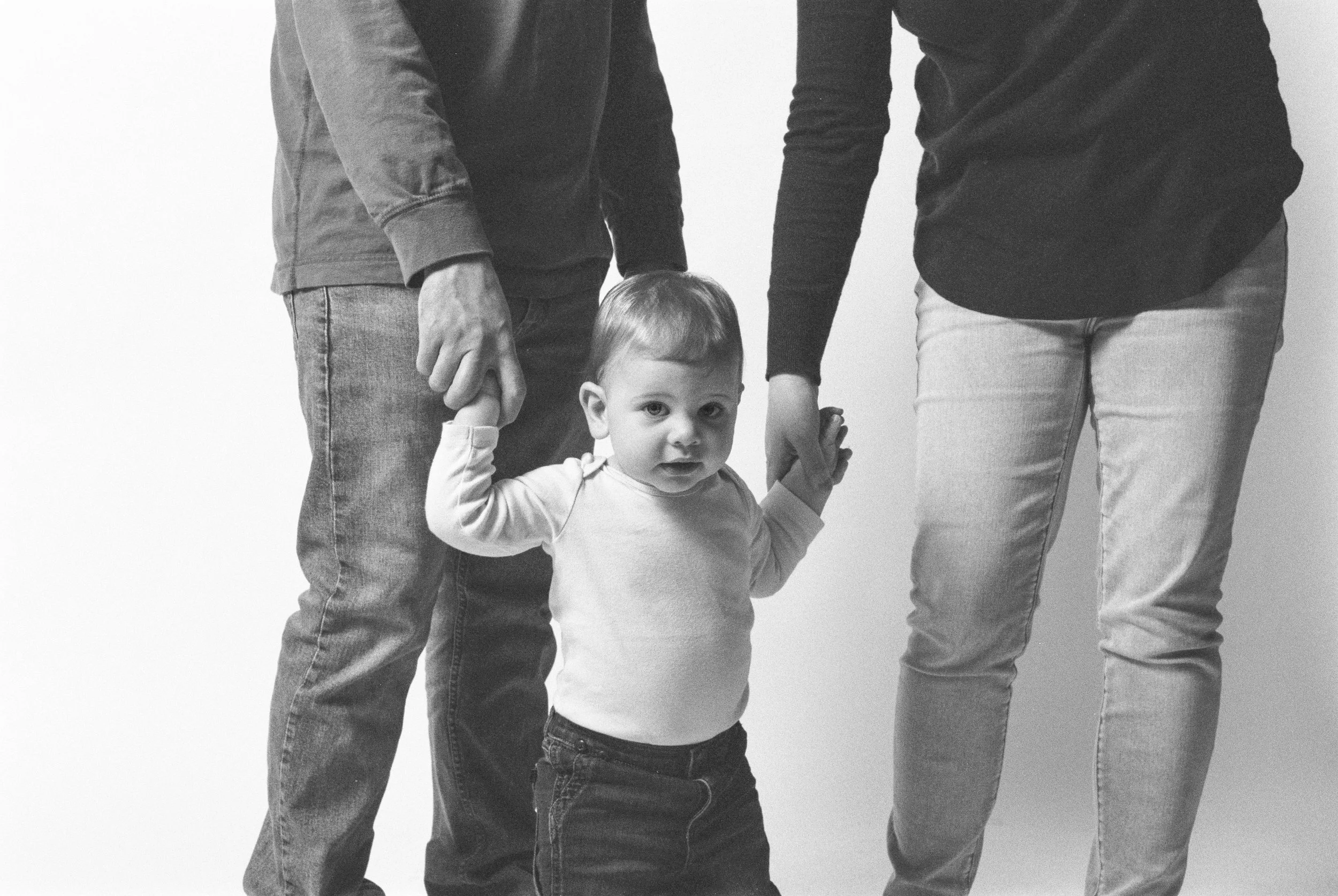 A young child holding adult hands on both sides, standing against a plain background.