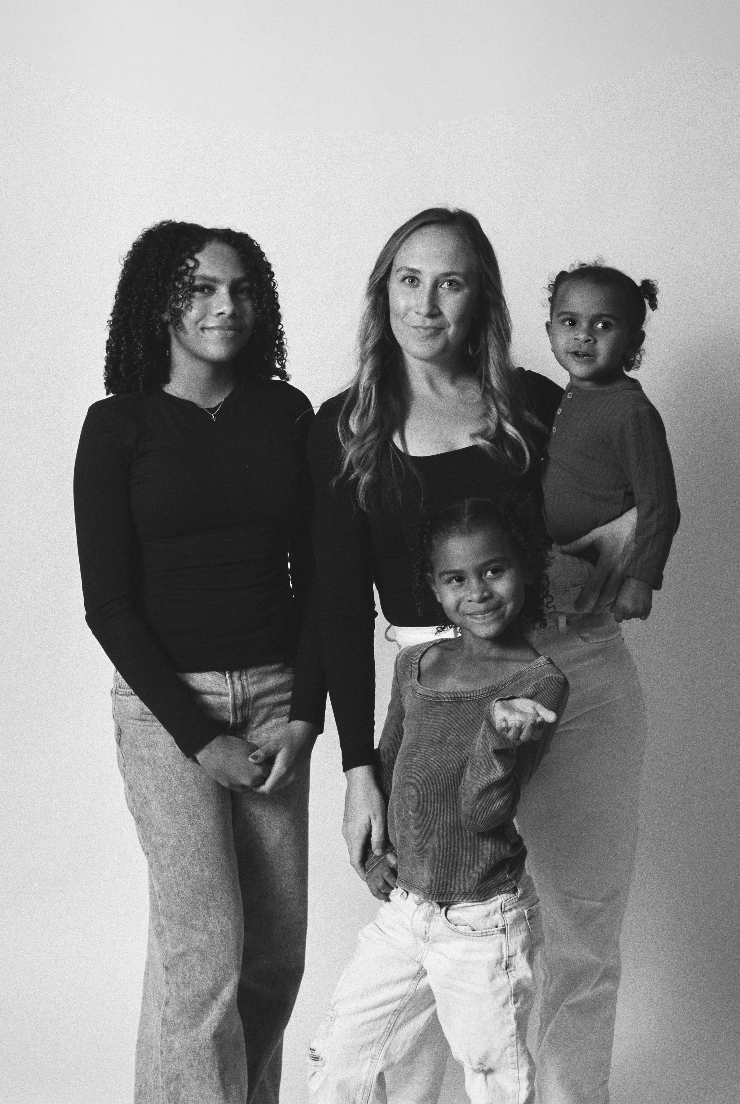 A group of four women and children standing together and smiling in a black-and-white photo.