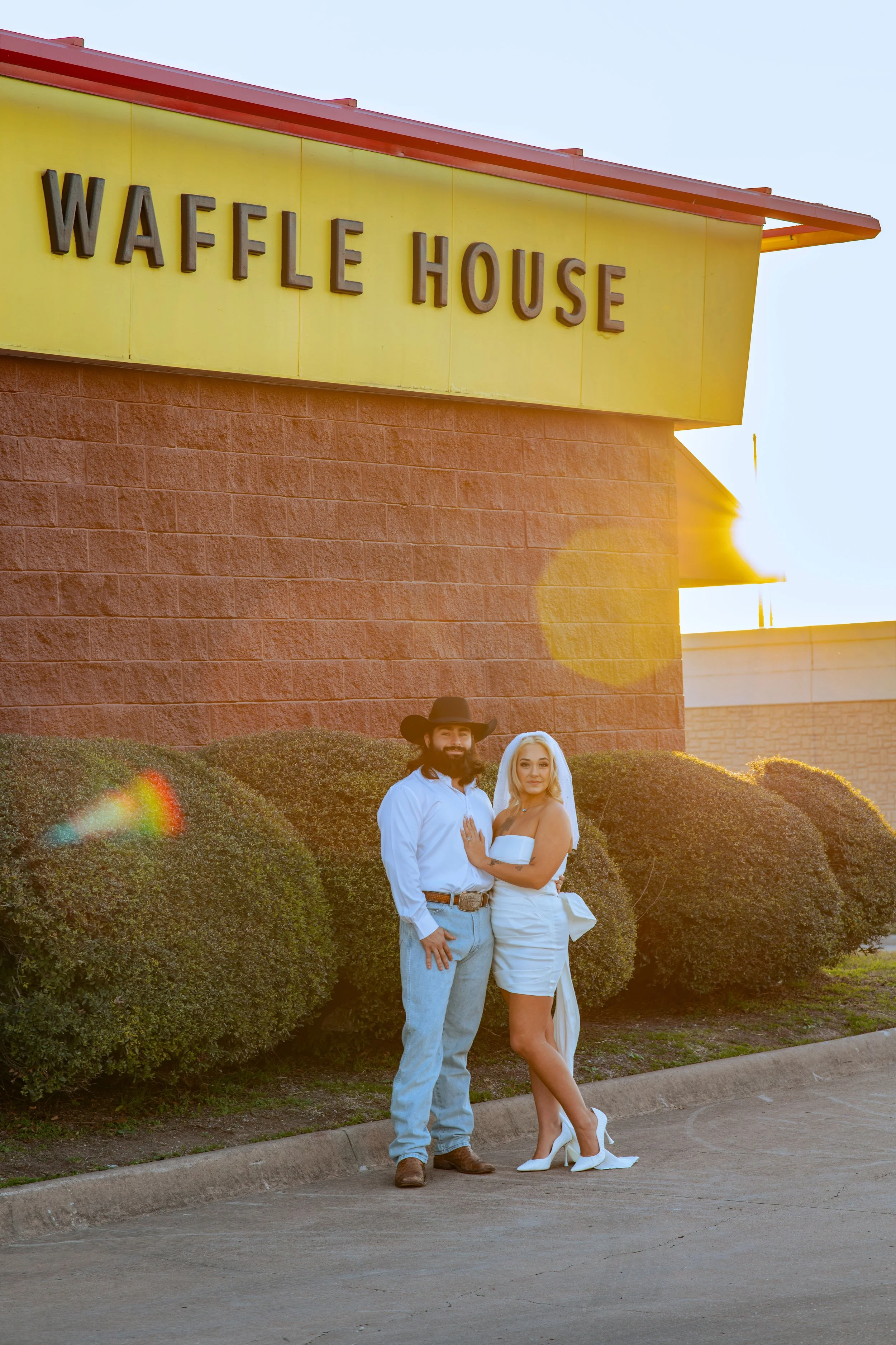 A couple dressed in western-style wedding attire standing outside Waffle House at sunset.
