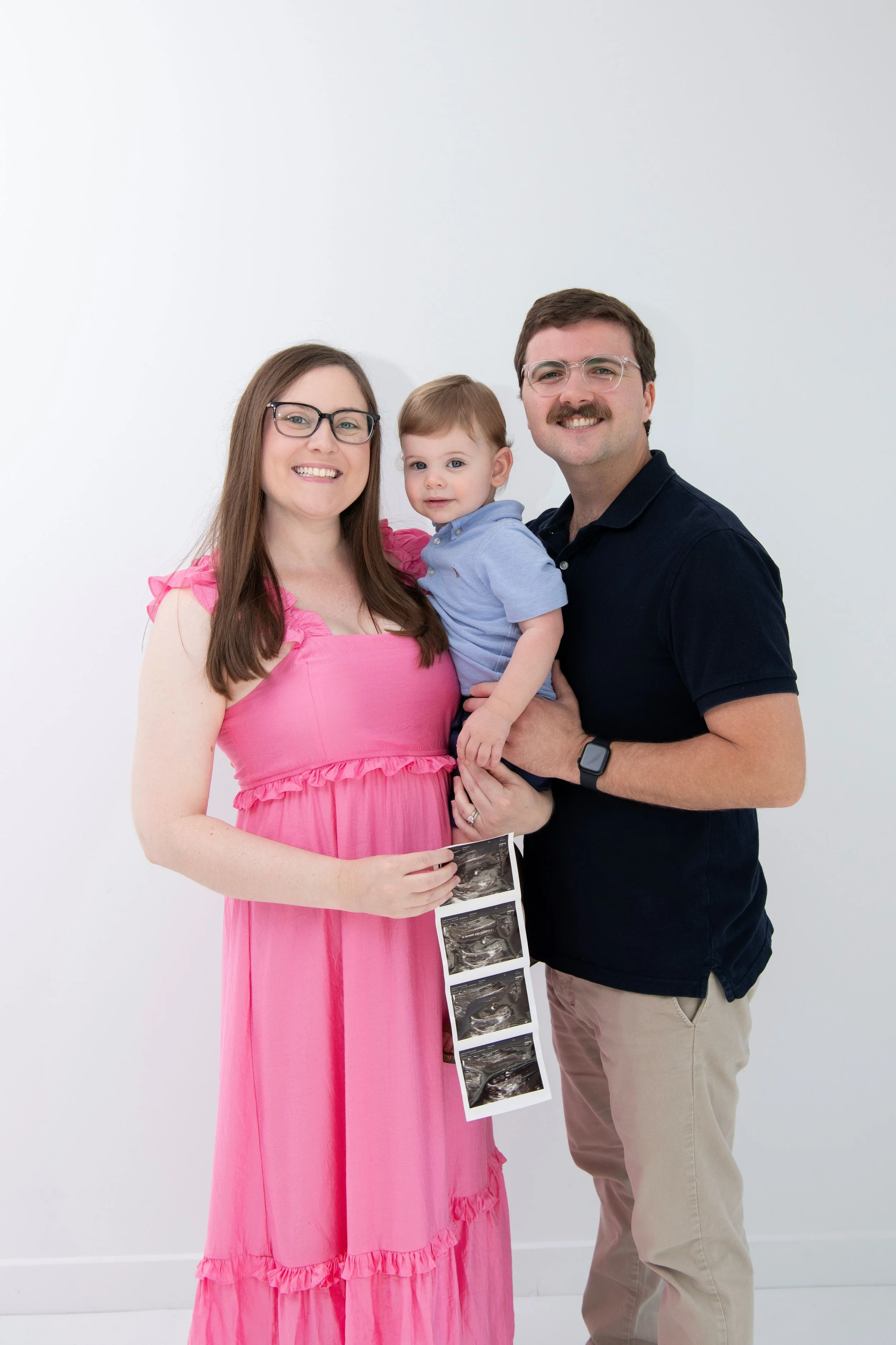 A couple with their toddler holding ultrasound images, celebrating pregnancy.