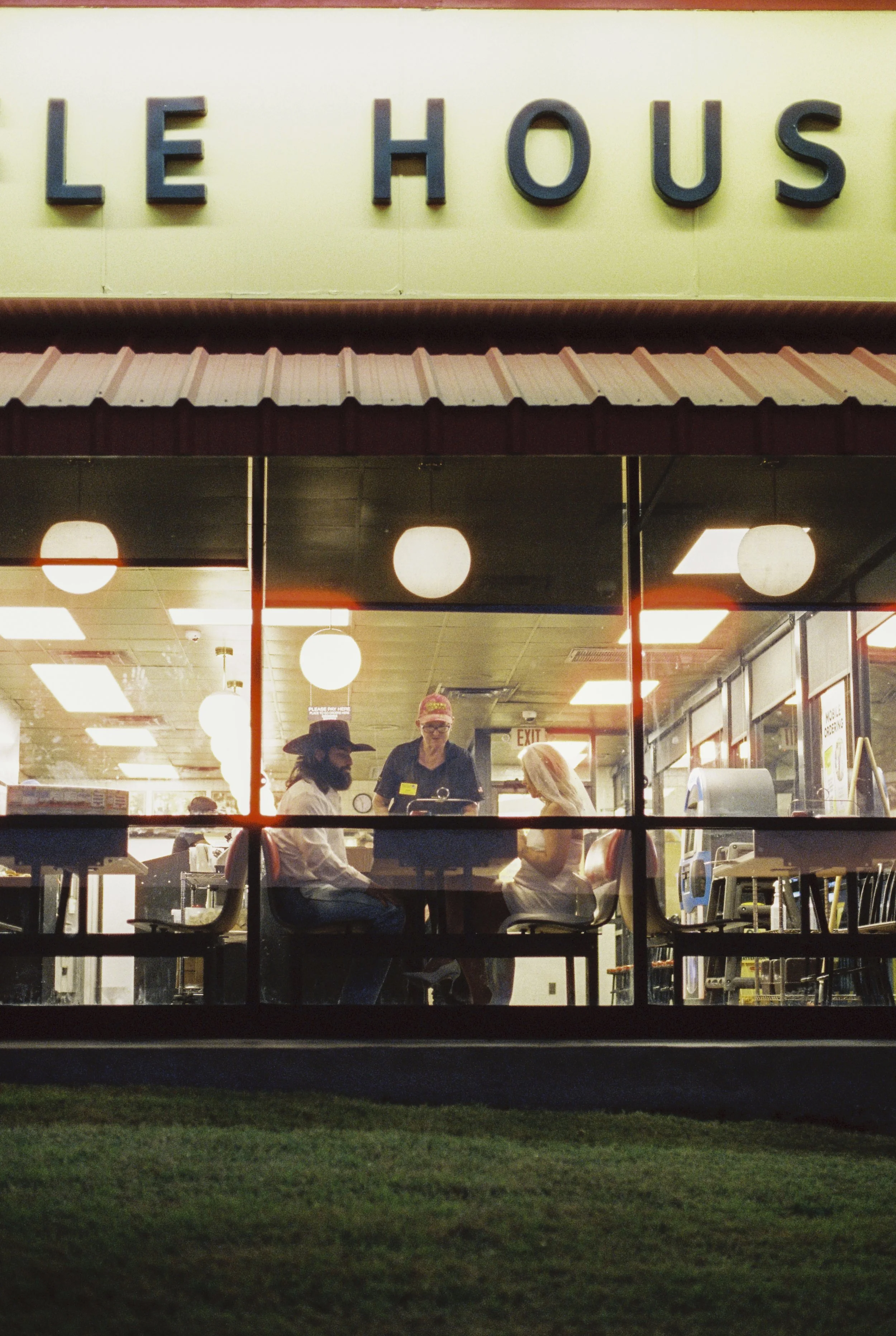 People sitting inside a restaurant called Le Haus, seen through a window at night.