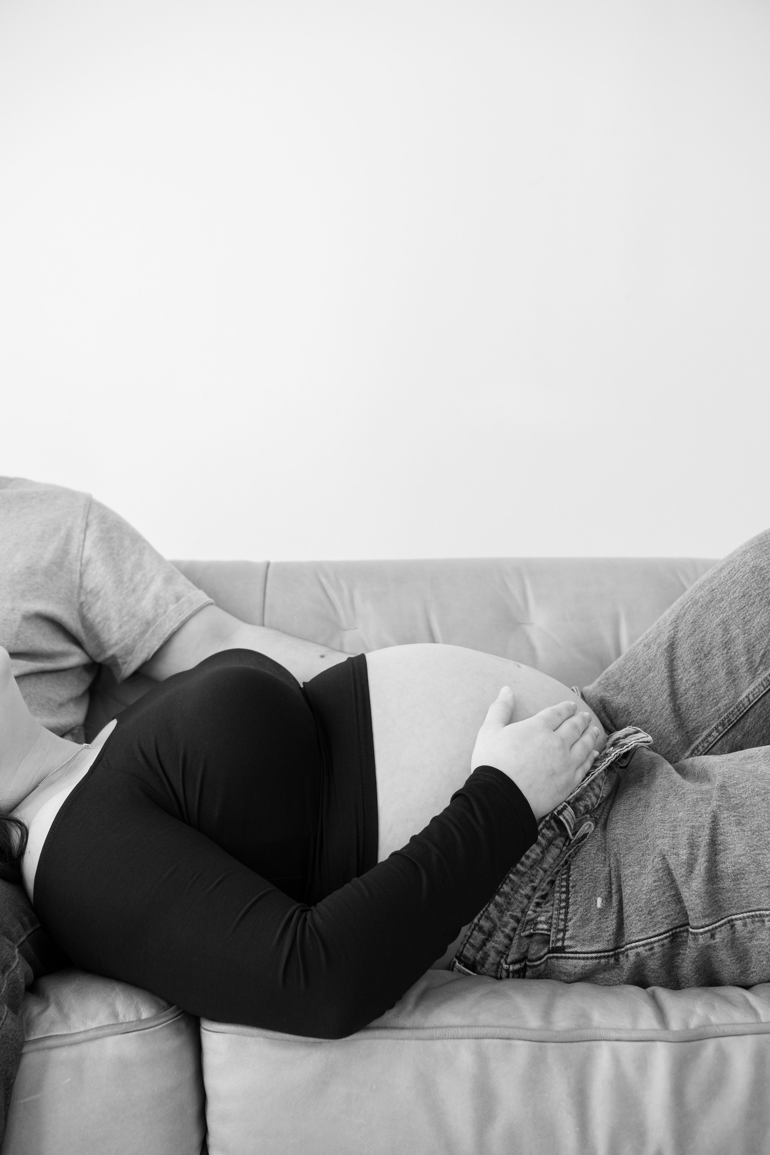 A pregnant woman lying on a couch with a man, her hand resting on her belly.