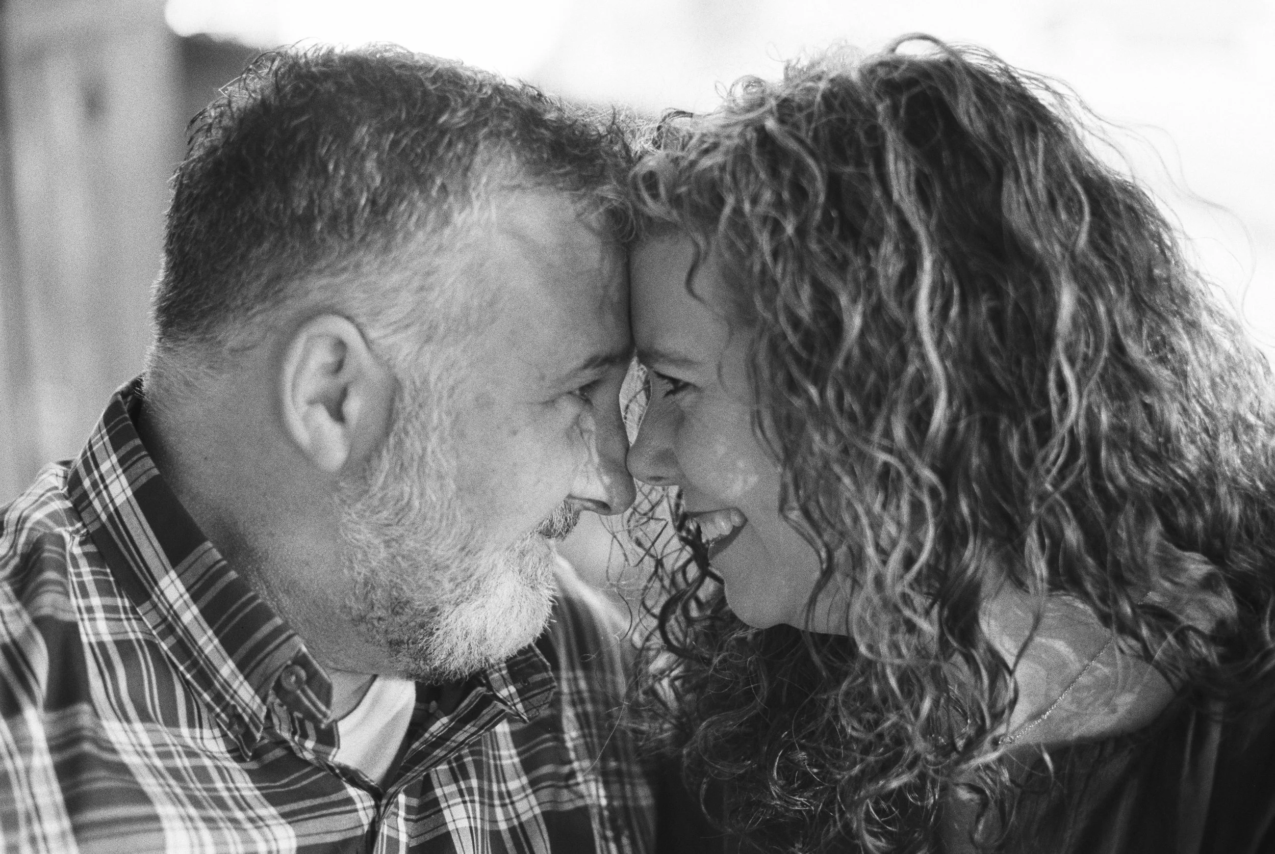 A close-up black and white photo of a middle-aged man and a woman touching foreheads, smiling, with their noses nearly touching, showing affection.