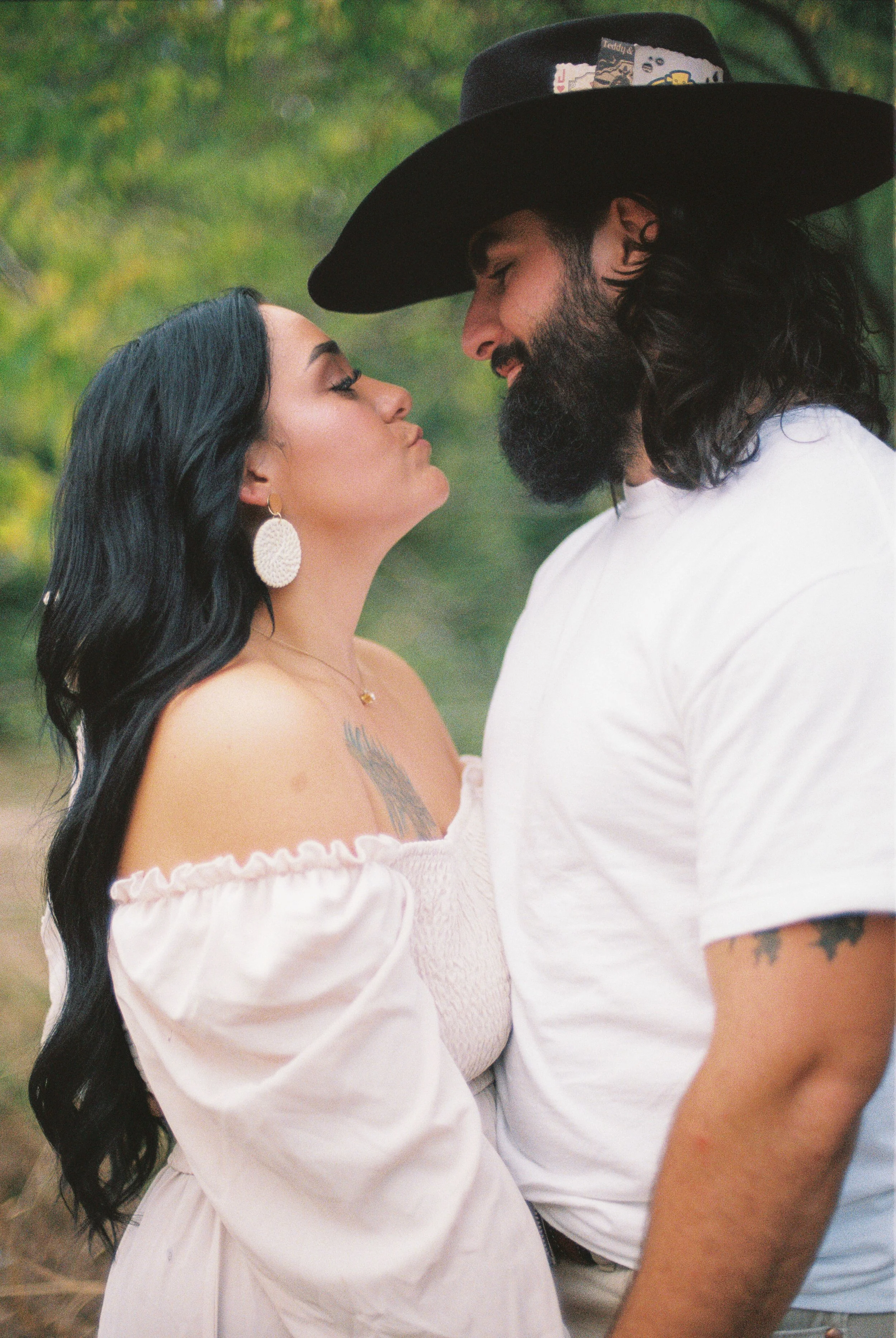 A man and woman standing close together outdoors, touching foreheads with eyes closed, in a gentle moment of affection.