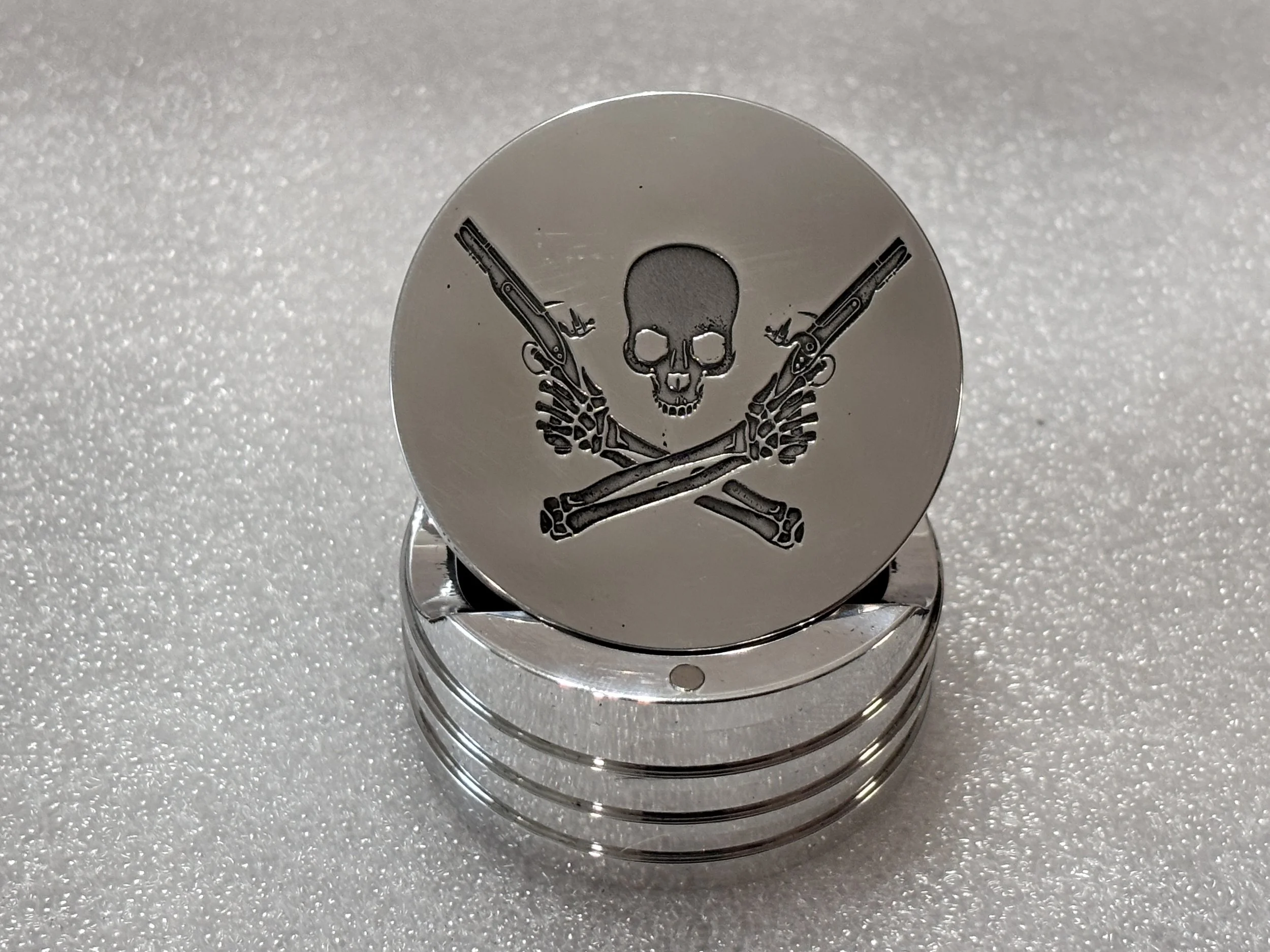 Stack of silver round objects with a skull and crossed guns design engraved on the top piece.