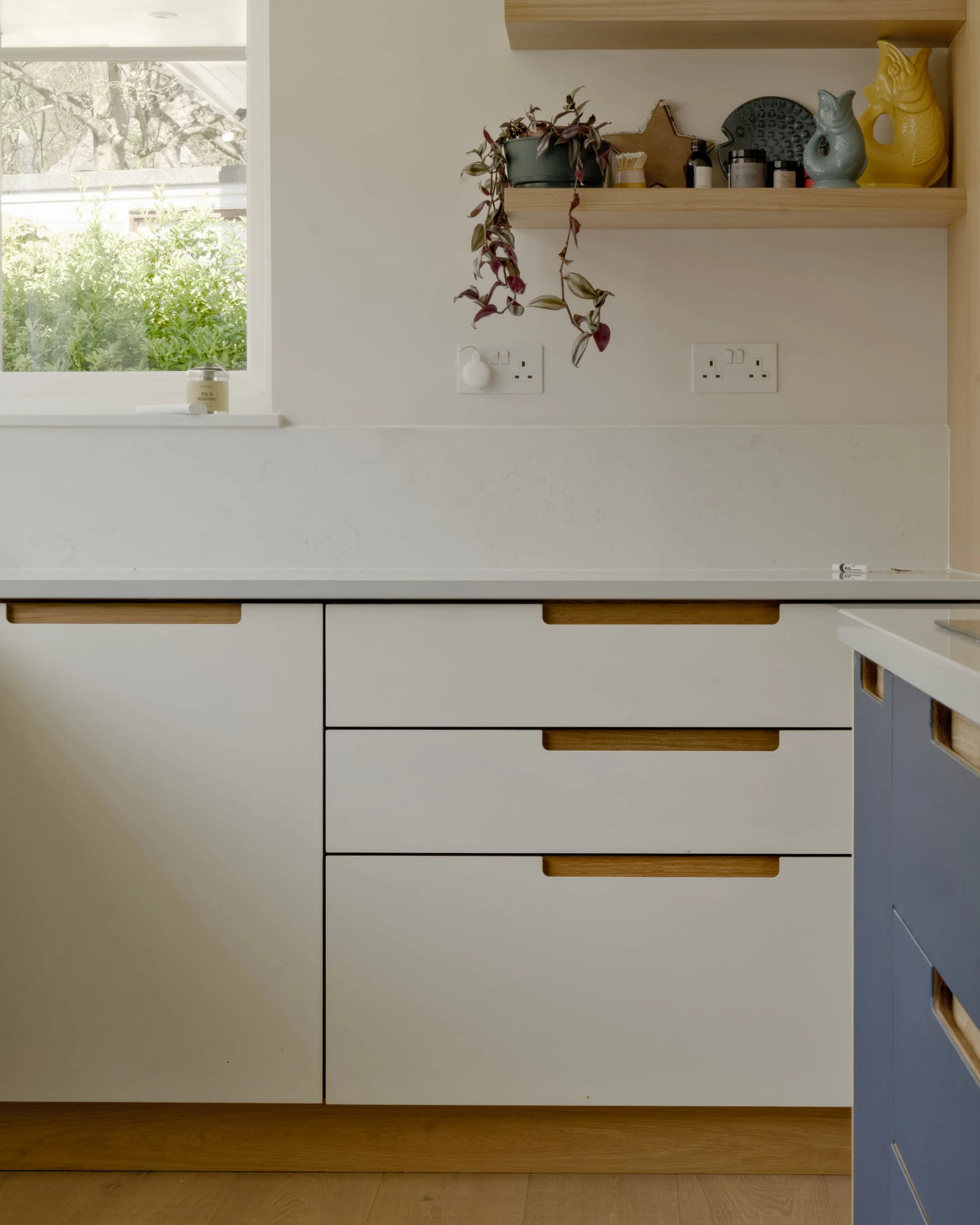 Corner of the kitchen where smokey blue and mushroom Forbo linoleum units meet beneath a white quartz worktop, with sash windows above