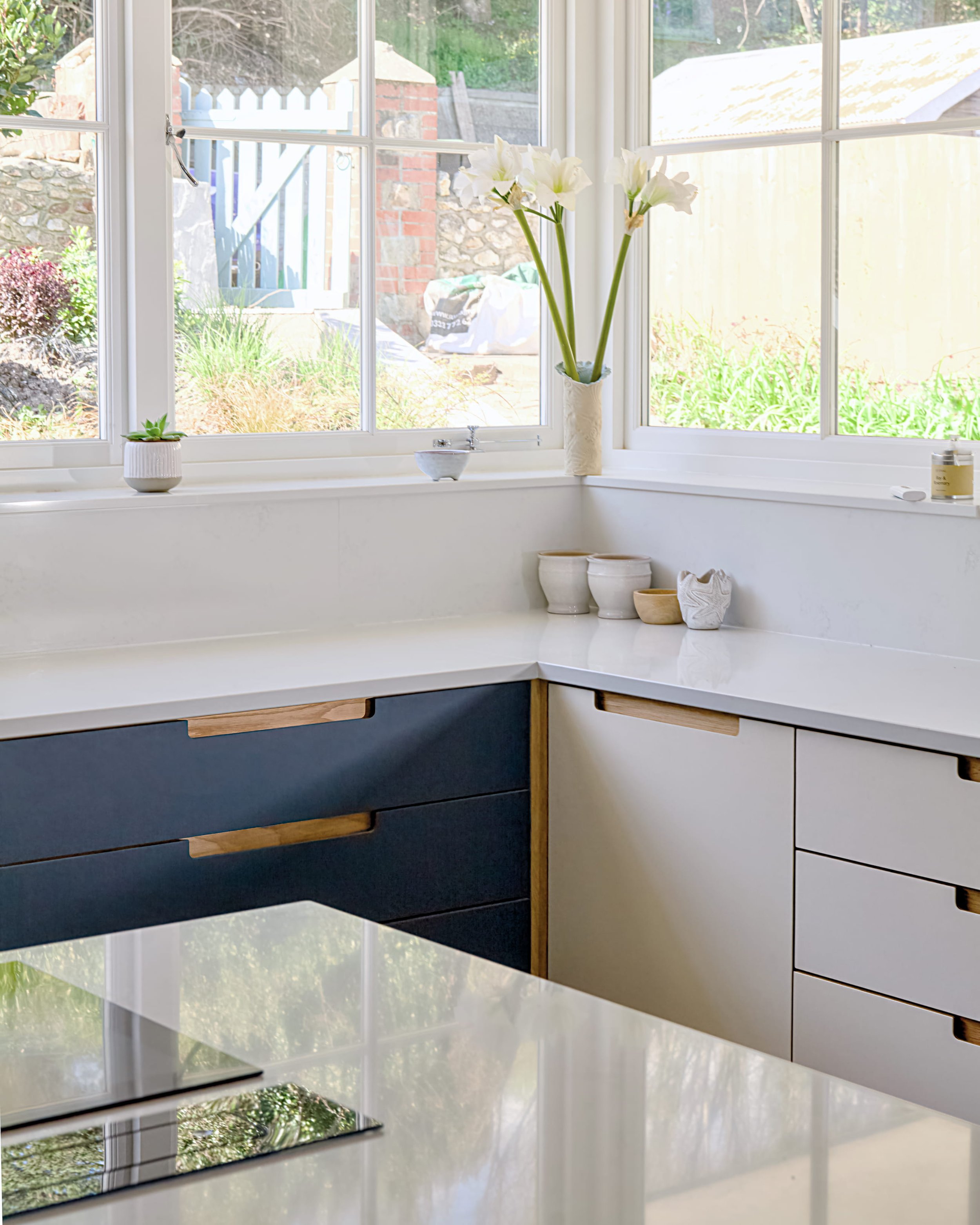 Corner of the kitchen where smokey blue and mushroom Forbo linoleum units meet beneath a white quartz worktop, with sash windows above