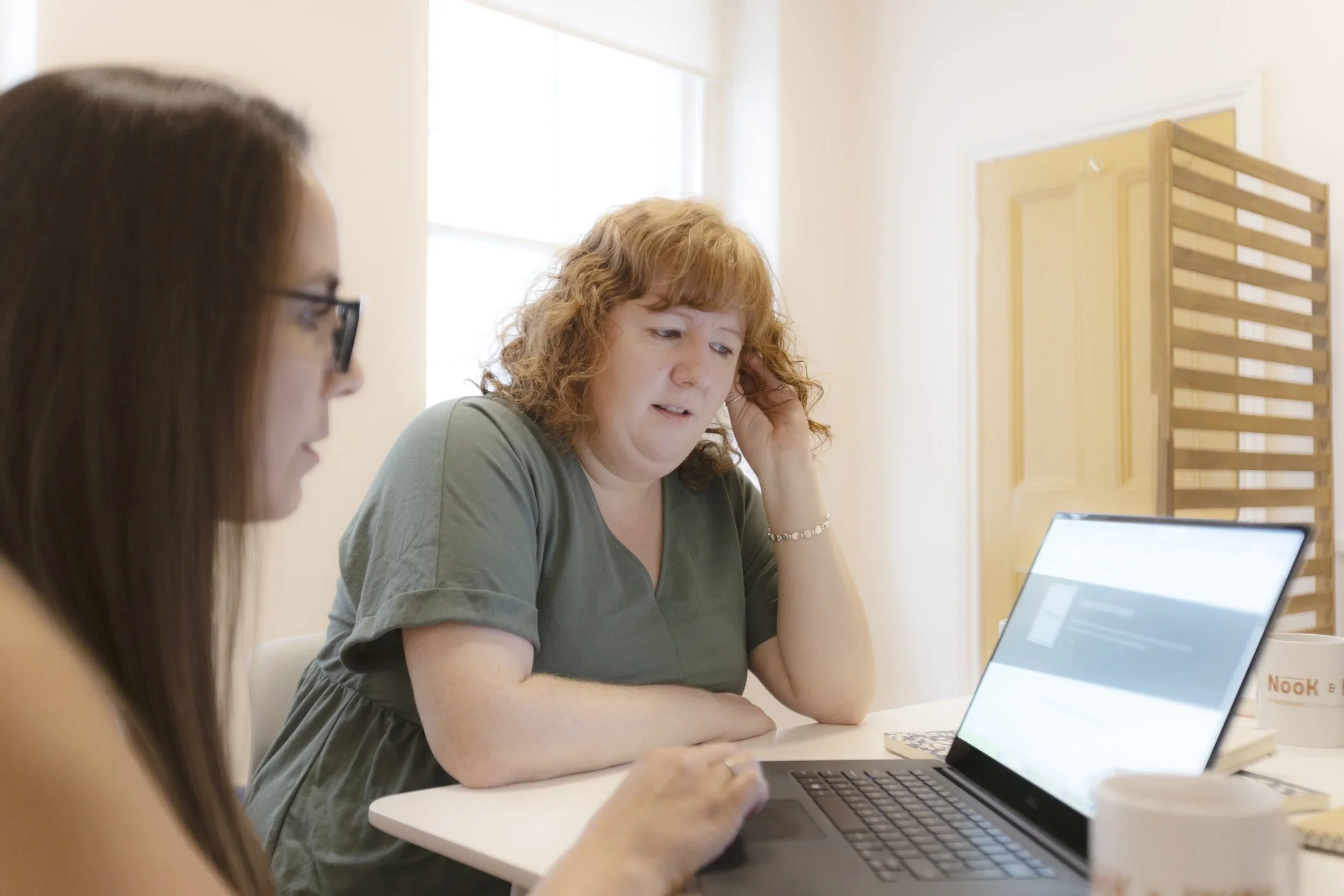 Two ladies sit together looking at a laptop screen.