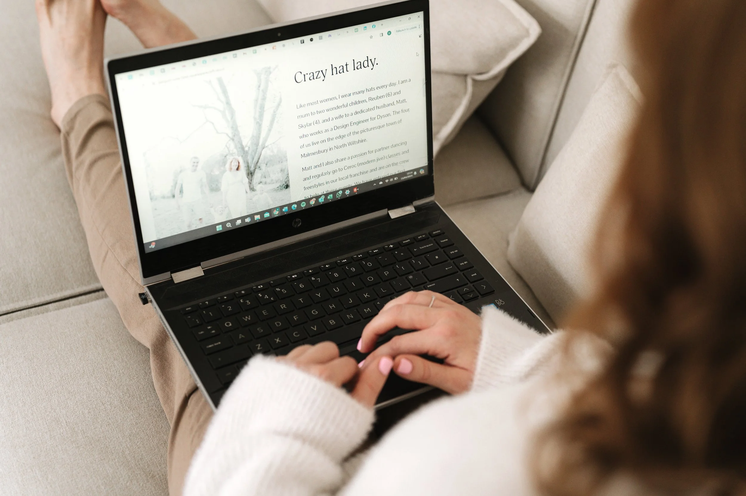 Person sitting on a beige couch using a black HP laptop with a website open displaying a blog post titled 'Crazy hat lady'.