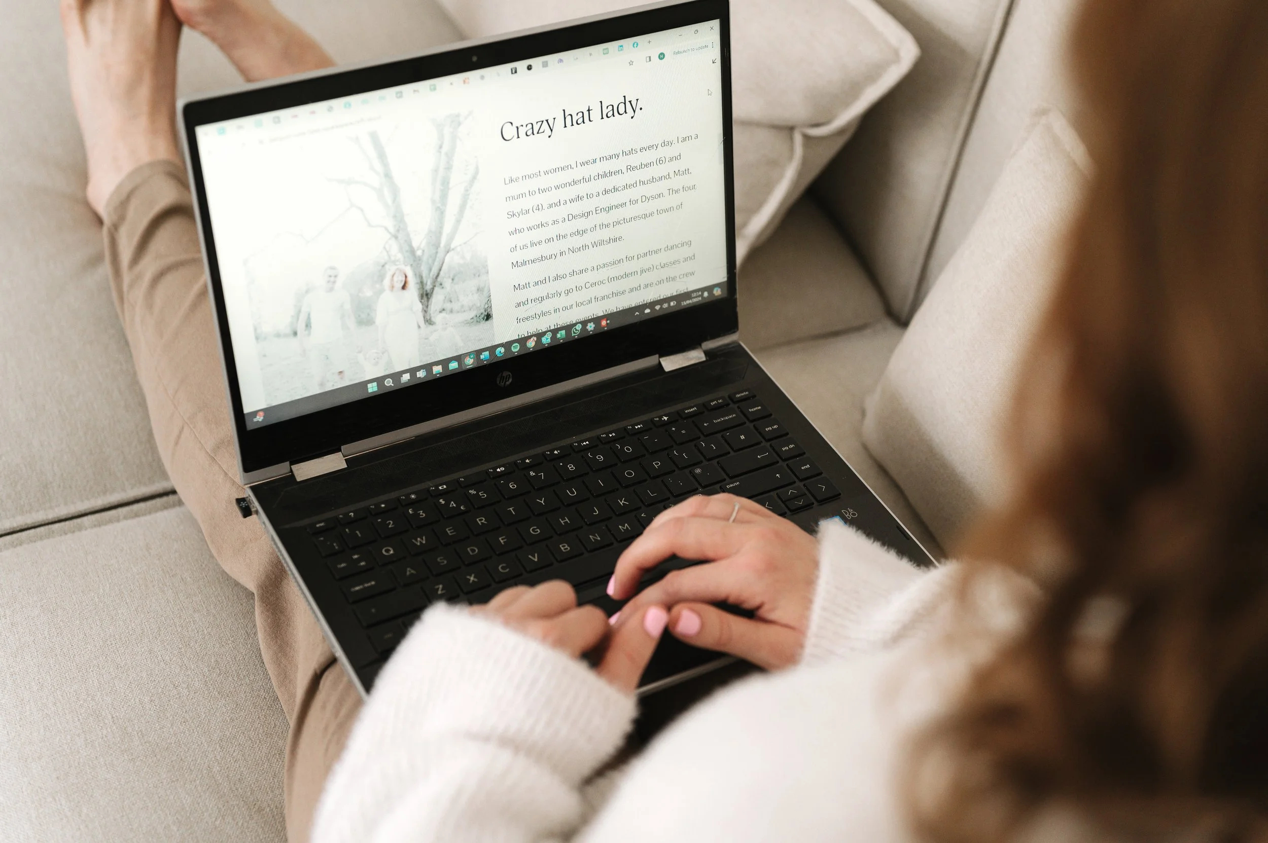 Close up of an open laptop on a lady's lap. Her hands rest on the keyboard.