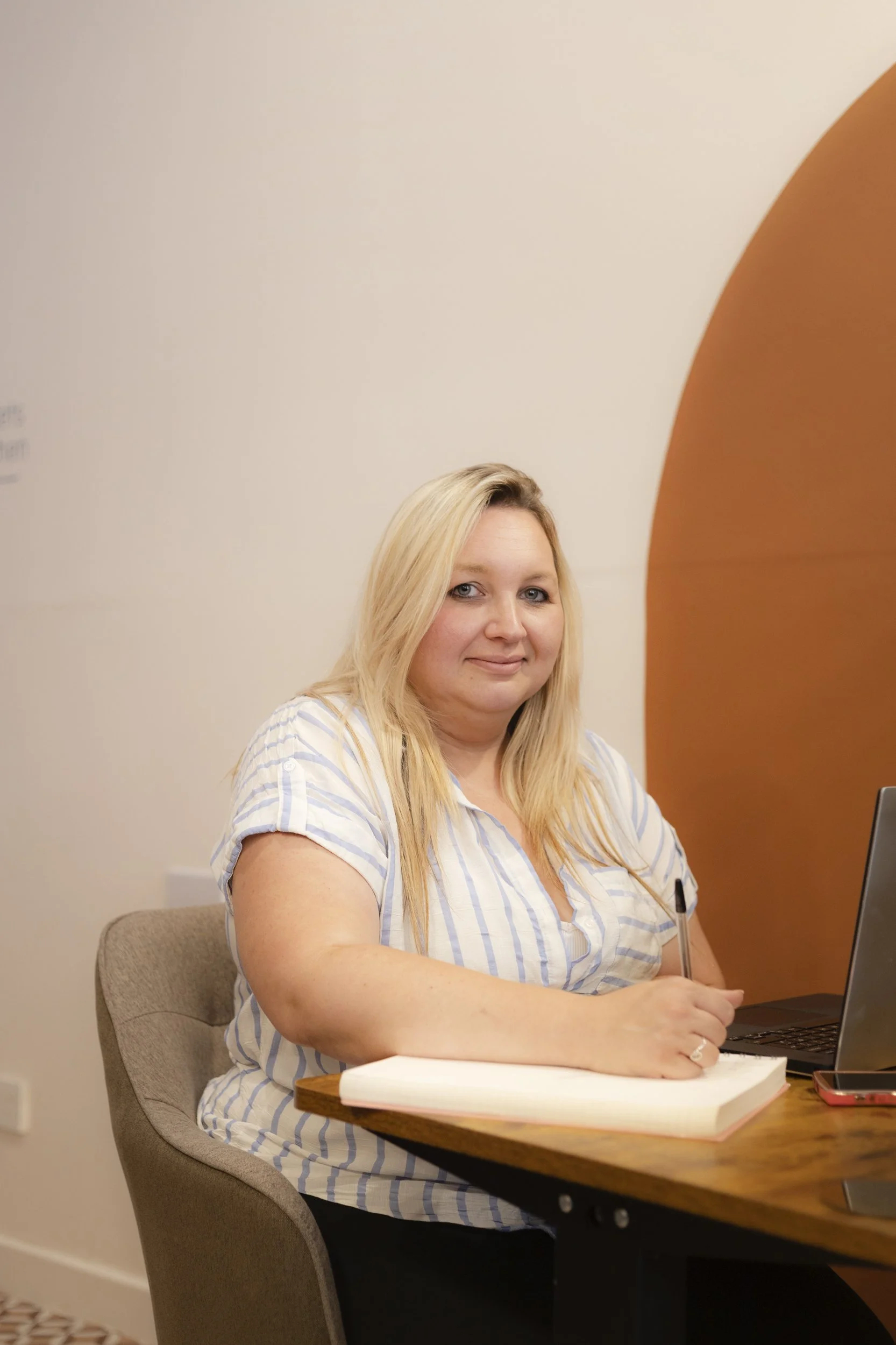 Grace, a woman with blonde hair, wearing a blue and white stripped shirt, smiles at the camera.