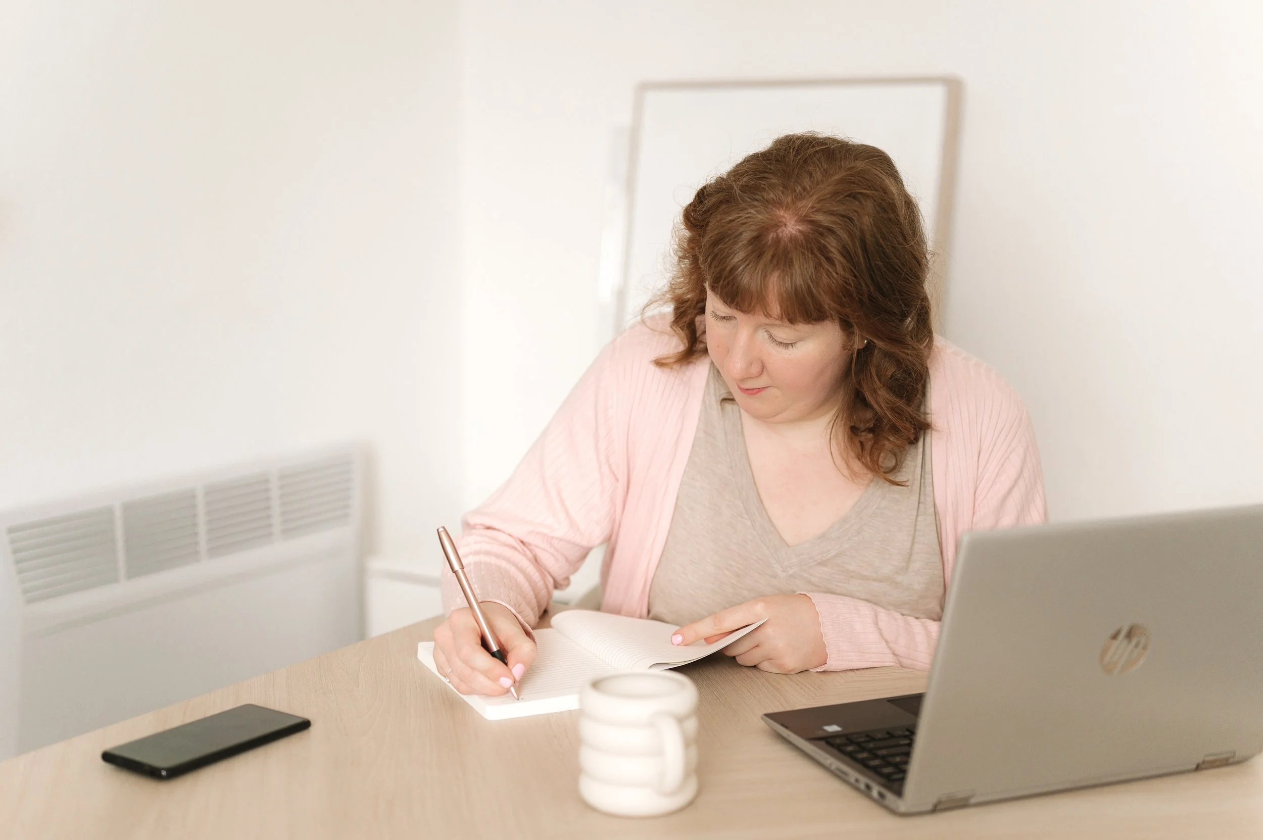 A lady sat at a desk writing notes in a notebook.